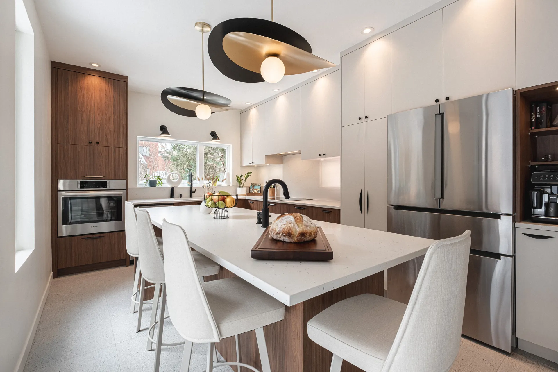 Cuisine moderne Menuitech avec armoires blanches et bois, comptoir blanc, îlot central, électroménagers inox et luminaires noirs