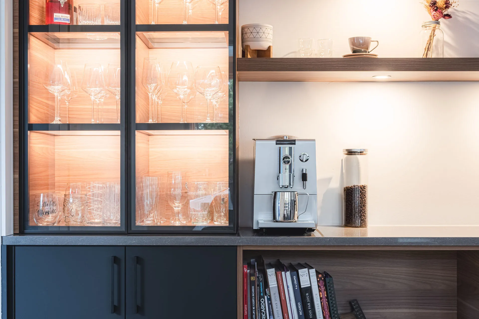 Black kitchen cabinets with lit glass doors, grey countertop, coffee machine, open wooden shelves in modern Montreal kitchen design