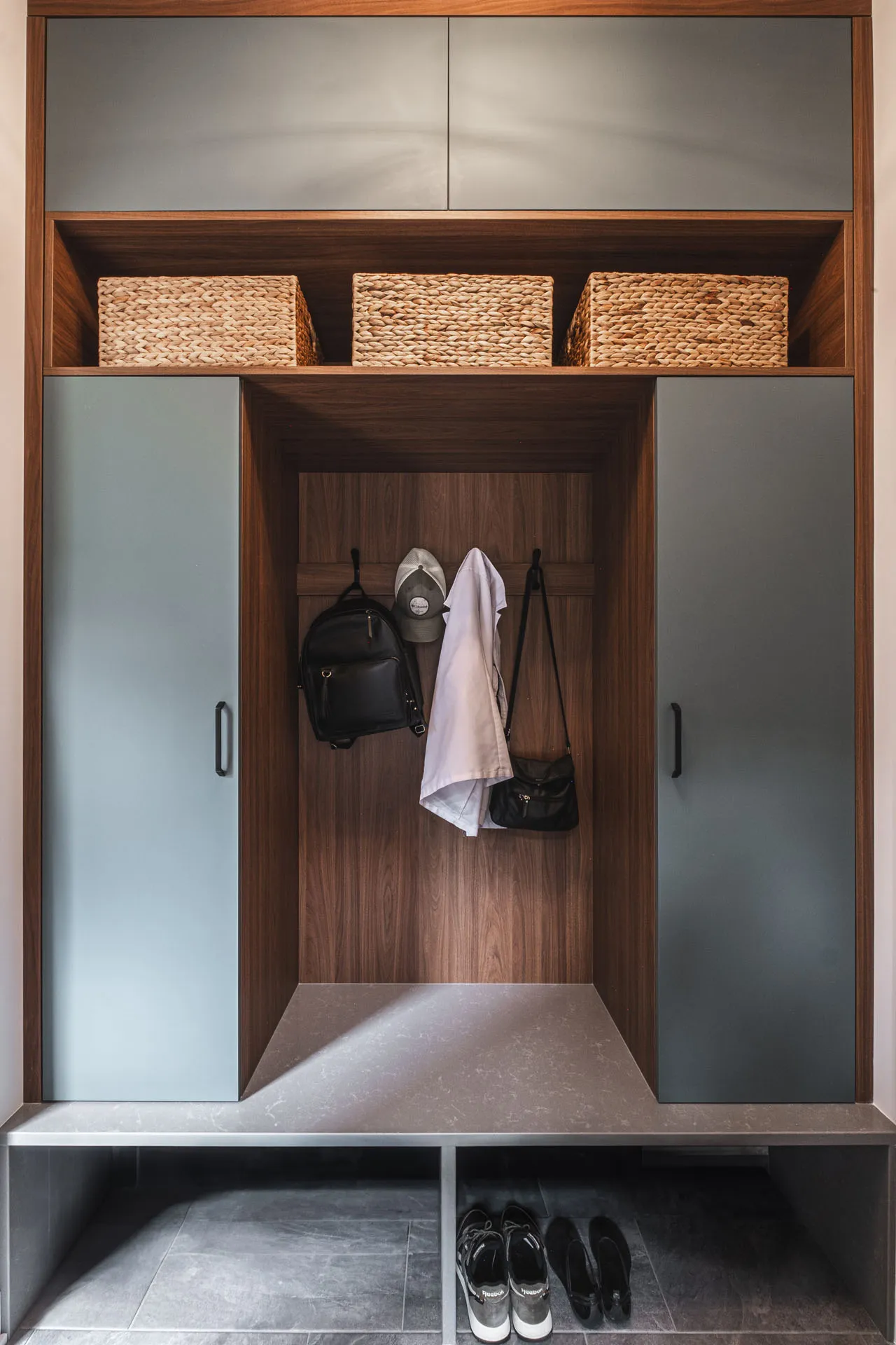 Custom Menuitech entryway: grey cabinets, wicker baskets, black hooks, shoe storage bench