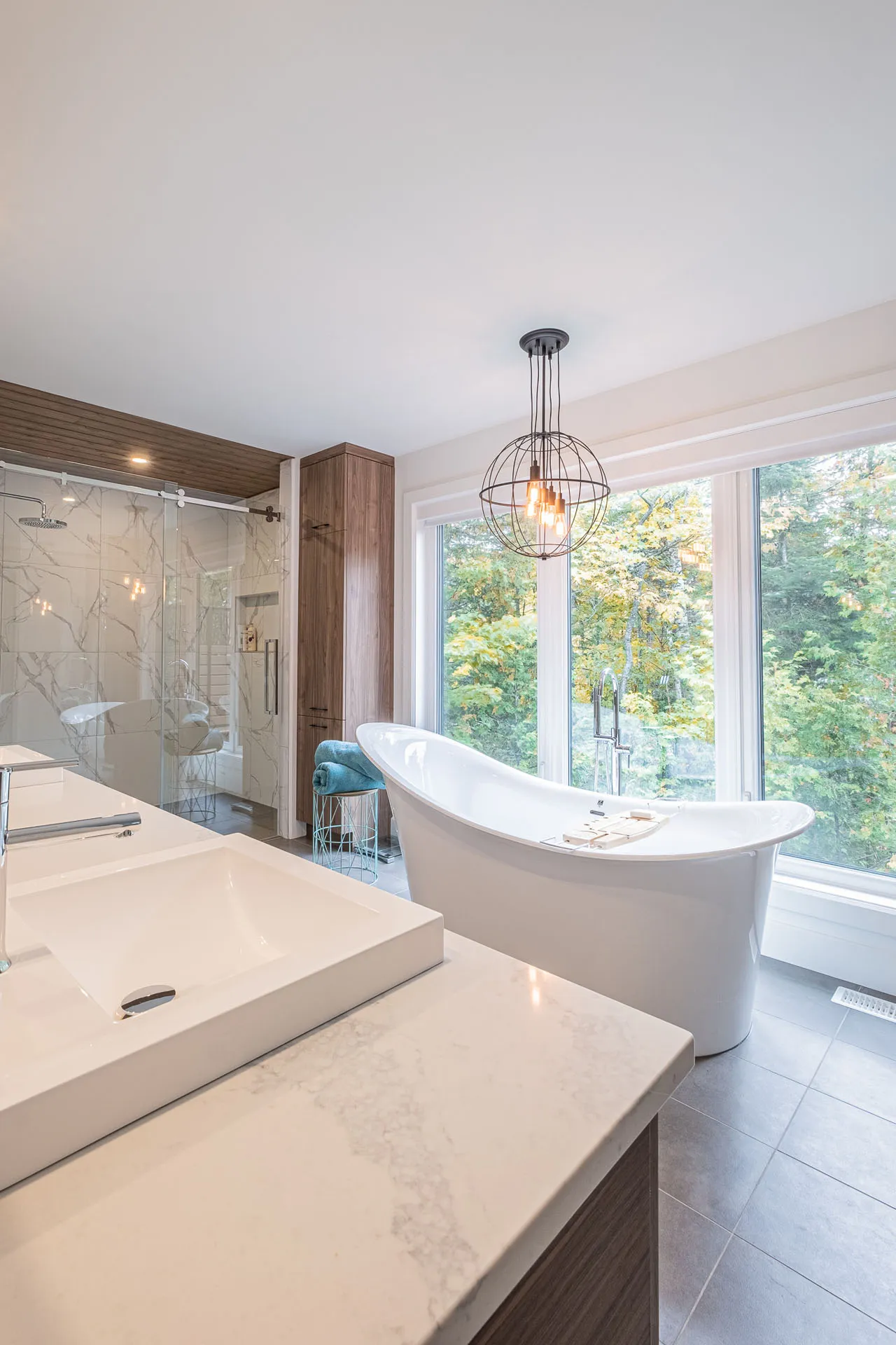Modern bathroom with marble double vanity, white soaking tub, wood cabinets, glass shower enclosure and pendant light