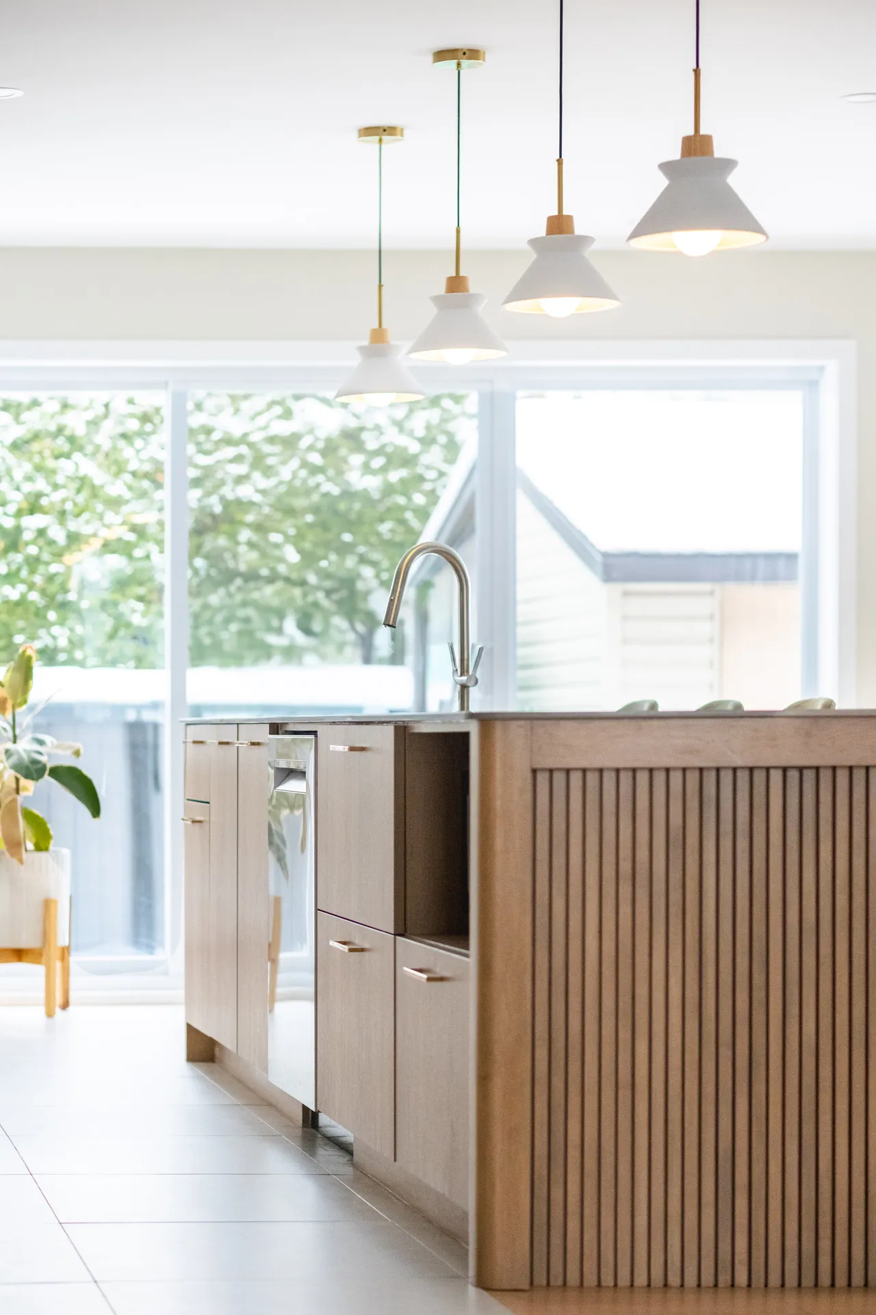 Cuisine moderne Menuitech avec armoires en bois clair, îlot avec comptoir gris, luminaires suspendus blanc et laiton