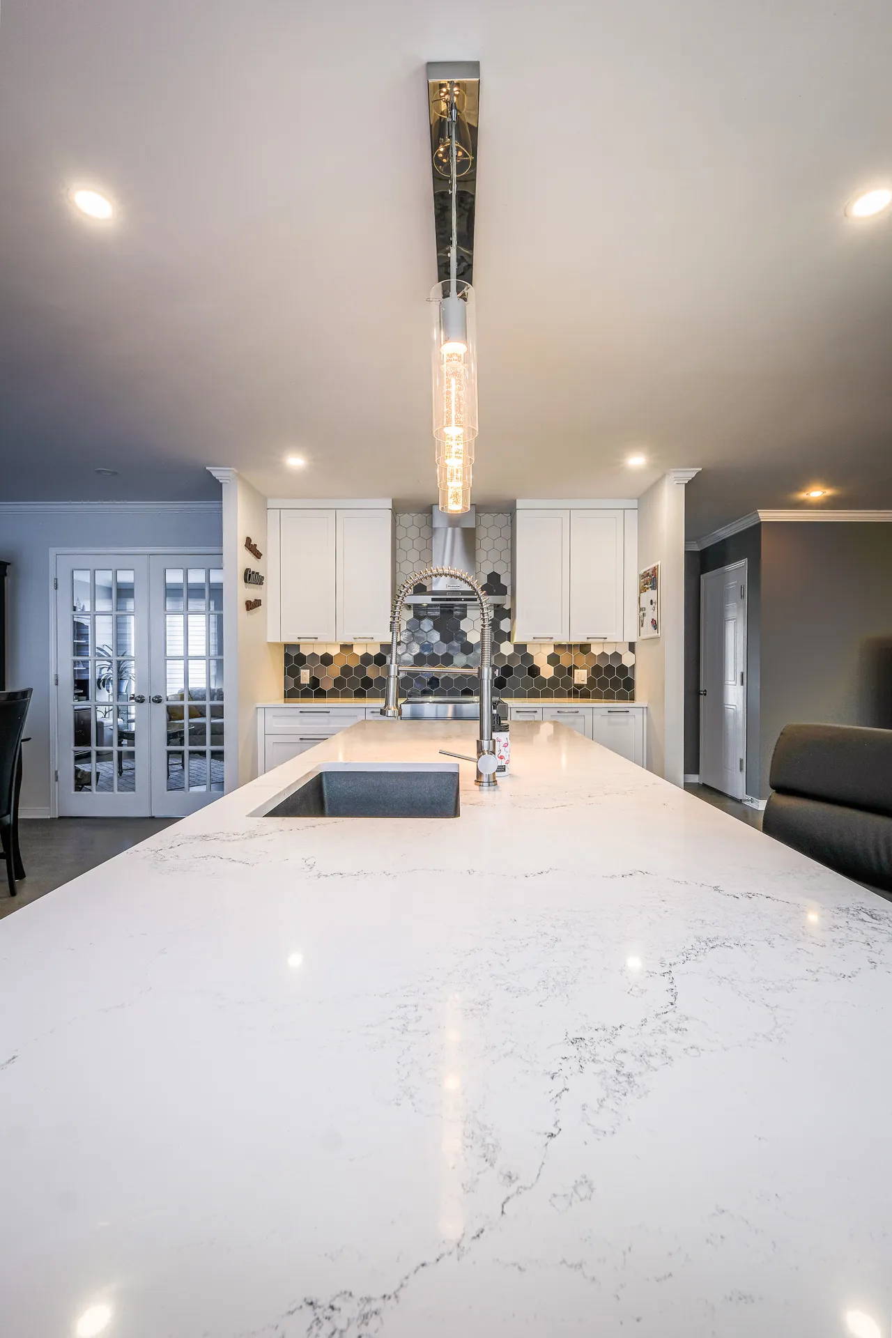 Landry kitchen Boisbriand: white cabinetry, marble countertop, island, black hexagonal backsplash, pendant light fixture.