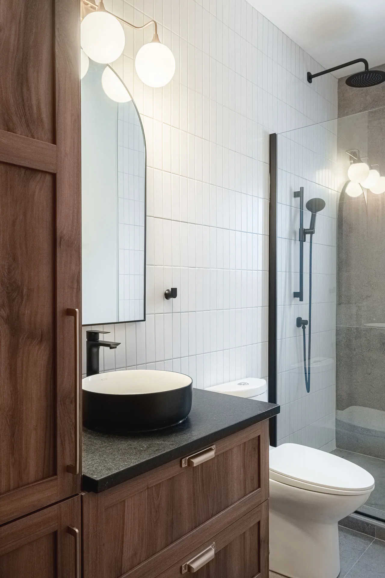 Modern bathroom with brown wood cabinets, grey countertop, round black vessel sink and glass shower enclosure