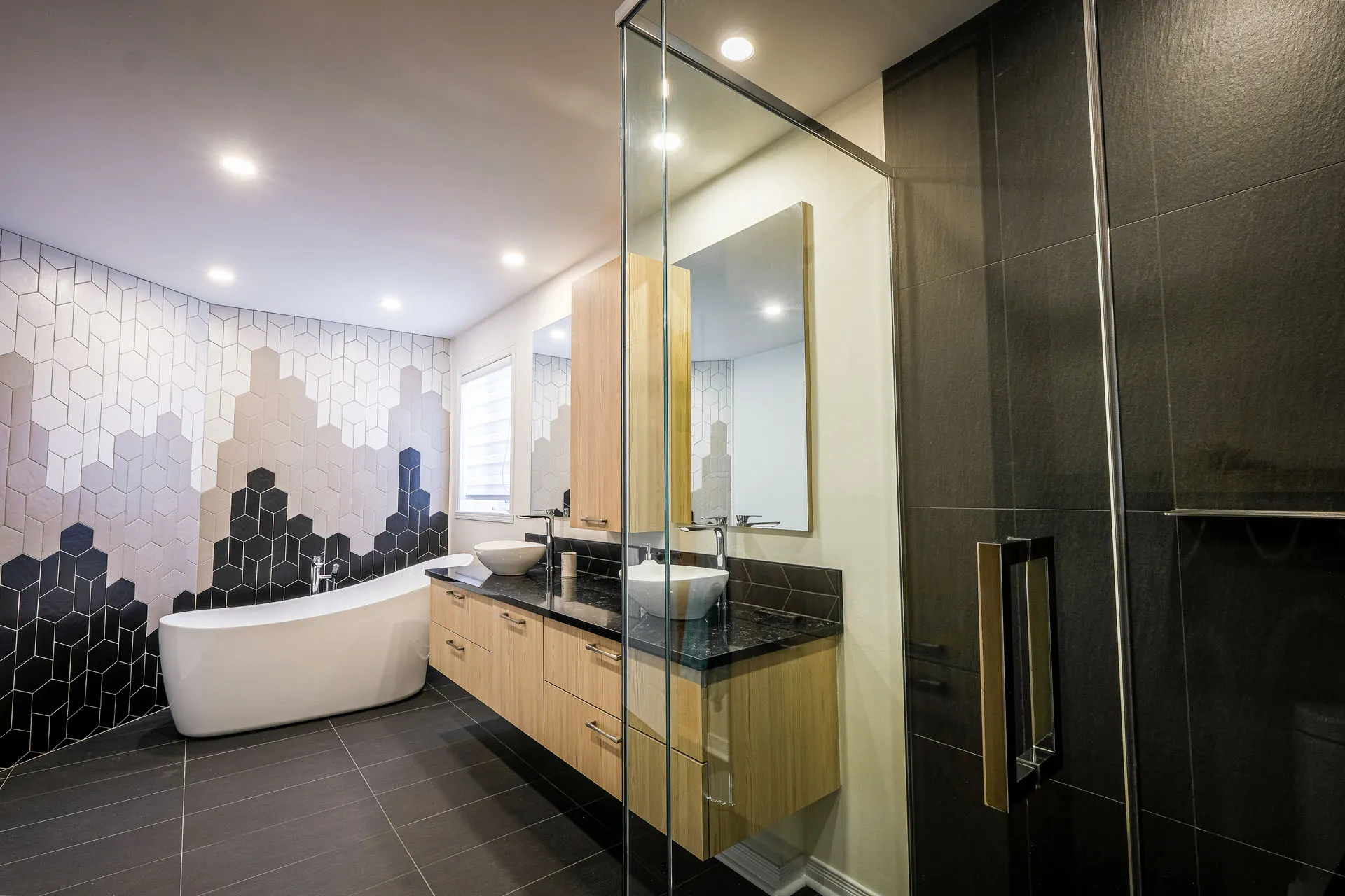 Modern Landry bathroom with oak cabinets, black countertop, geometric black and white backsplash, freestanding soaking tub
