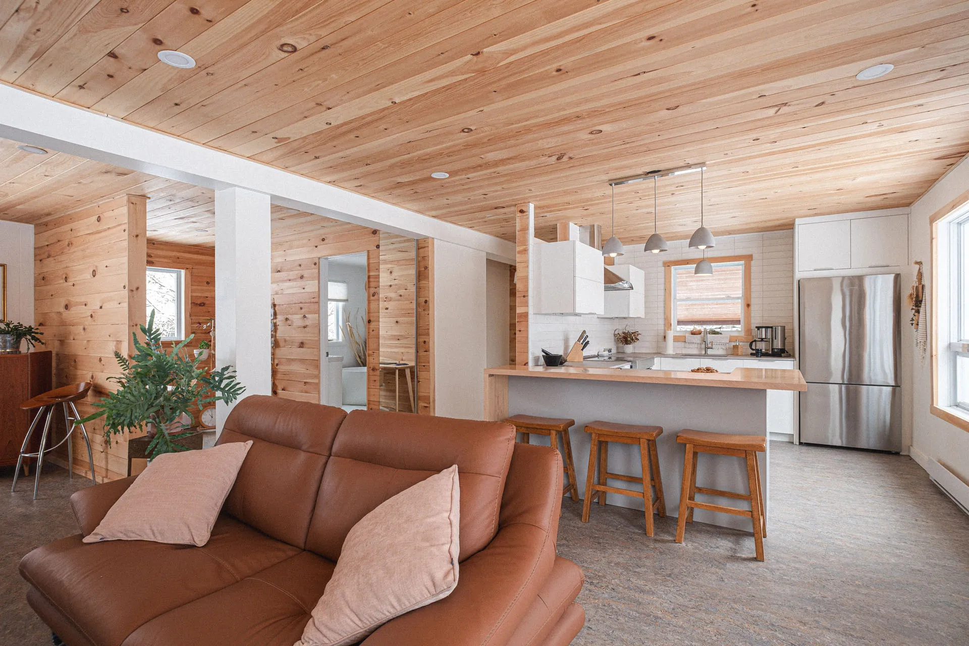 Open-concept modern kitchen with white cabinetry, light wood countertop, island, white backsplash and gray pendant lights.