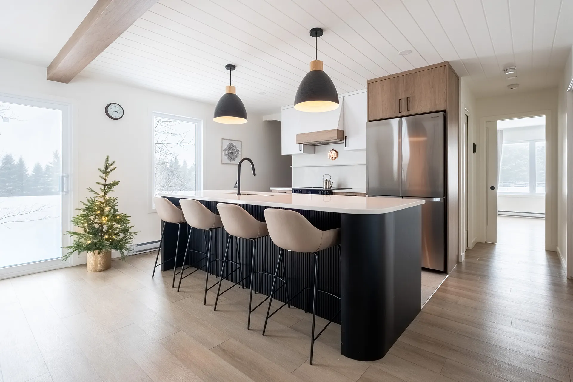 Cuisine moderne Alarie avec îlot noir, comptoirs blancs, armoires chêne, pendentifs noirs et électroménagers inox