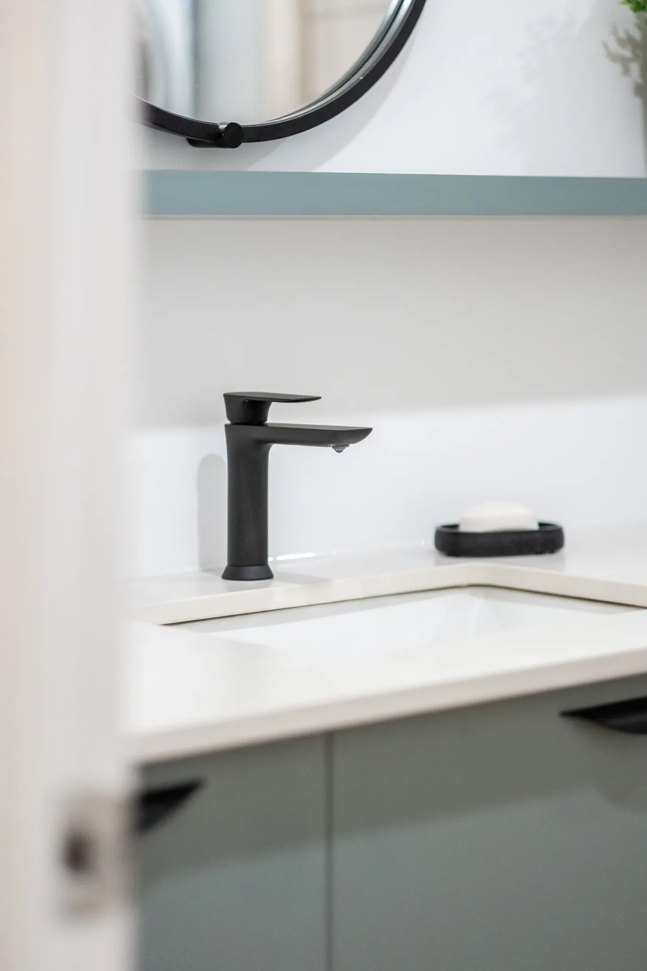 Salle de bain moderne avec vanité grise, comptoir blanc, robinet noir minimaliste et miroir rond