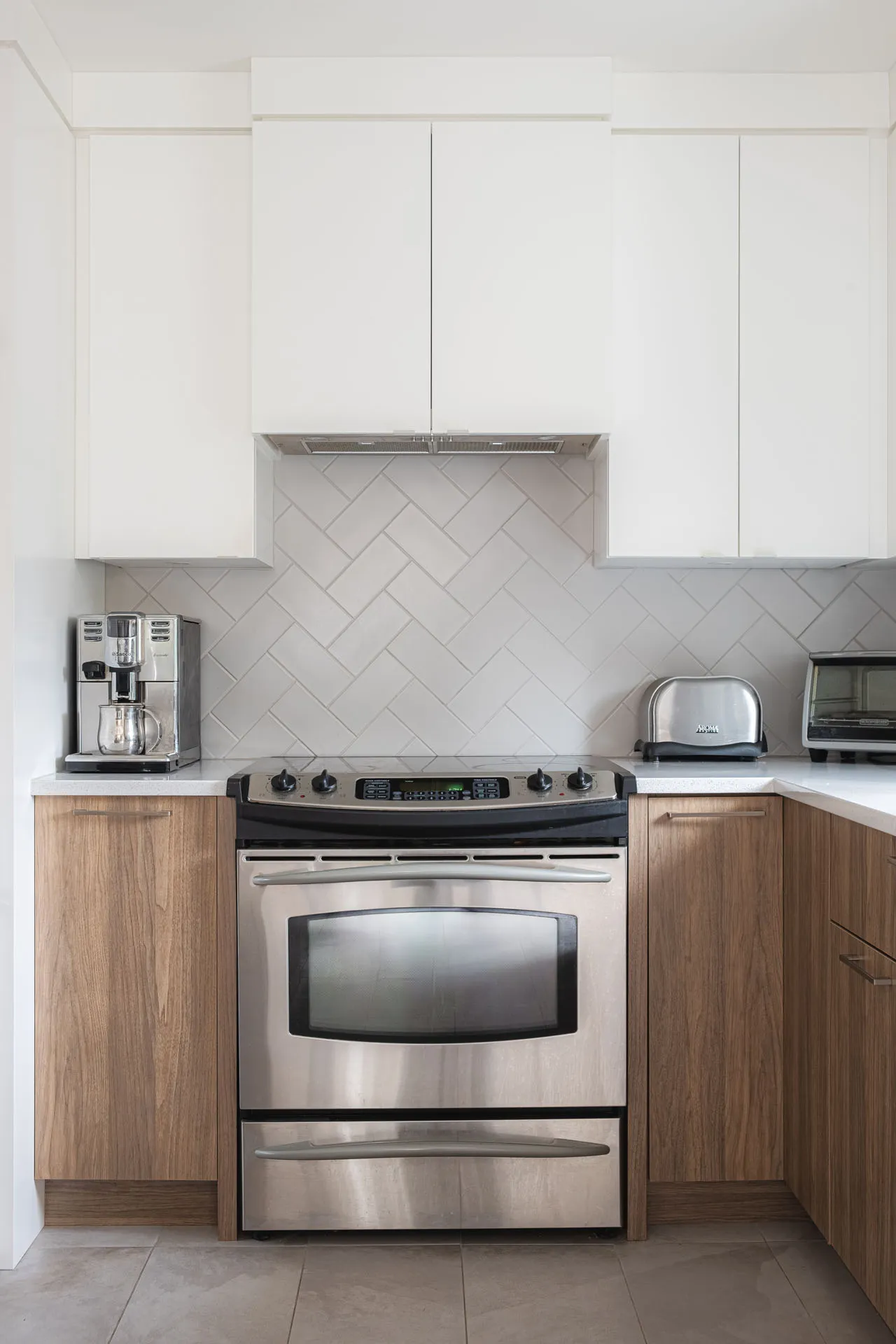 Modern Rosemère kitchen: natural wood cabinets, white countertop, herringbone tile backsplash, stainless steel appliances
