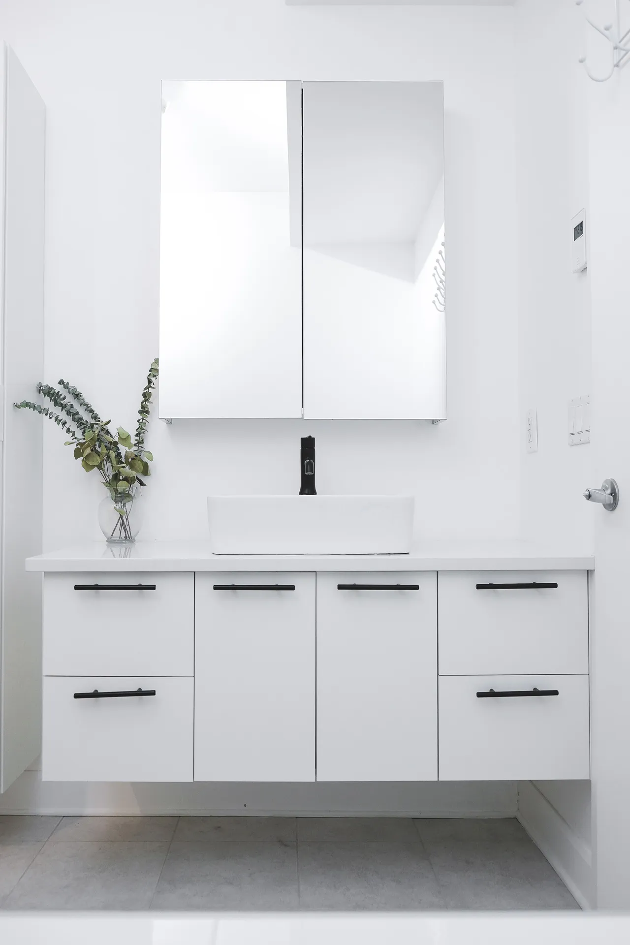 Modern bathroom with white vanity drawers, white countertop, framed mirror and black faucet fixtures
