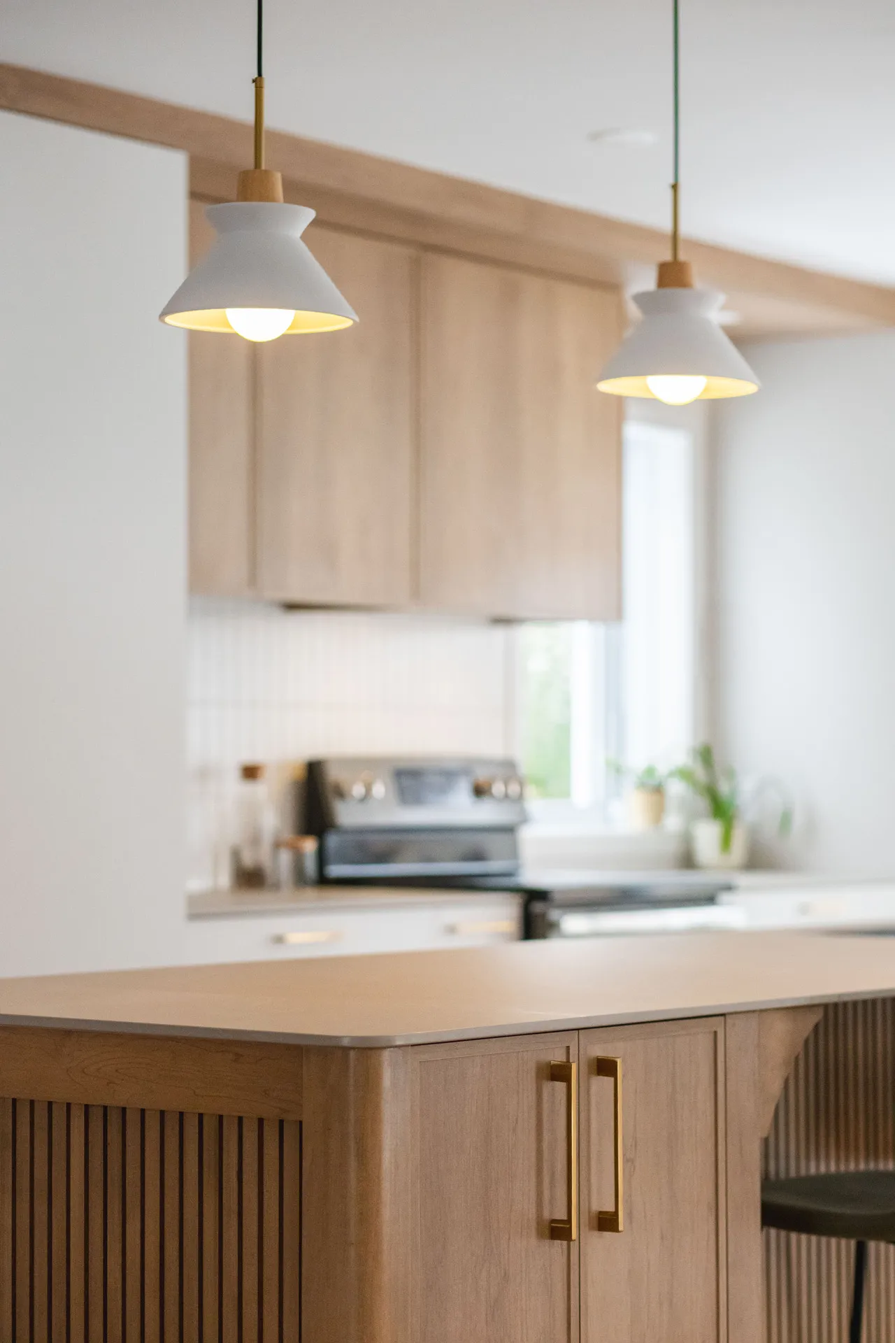 Cuisine Léveillé Blainville : armoires bois naturel, comptoir beige, îlot, dosseret blanc, luminaires suspendus blancs.