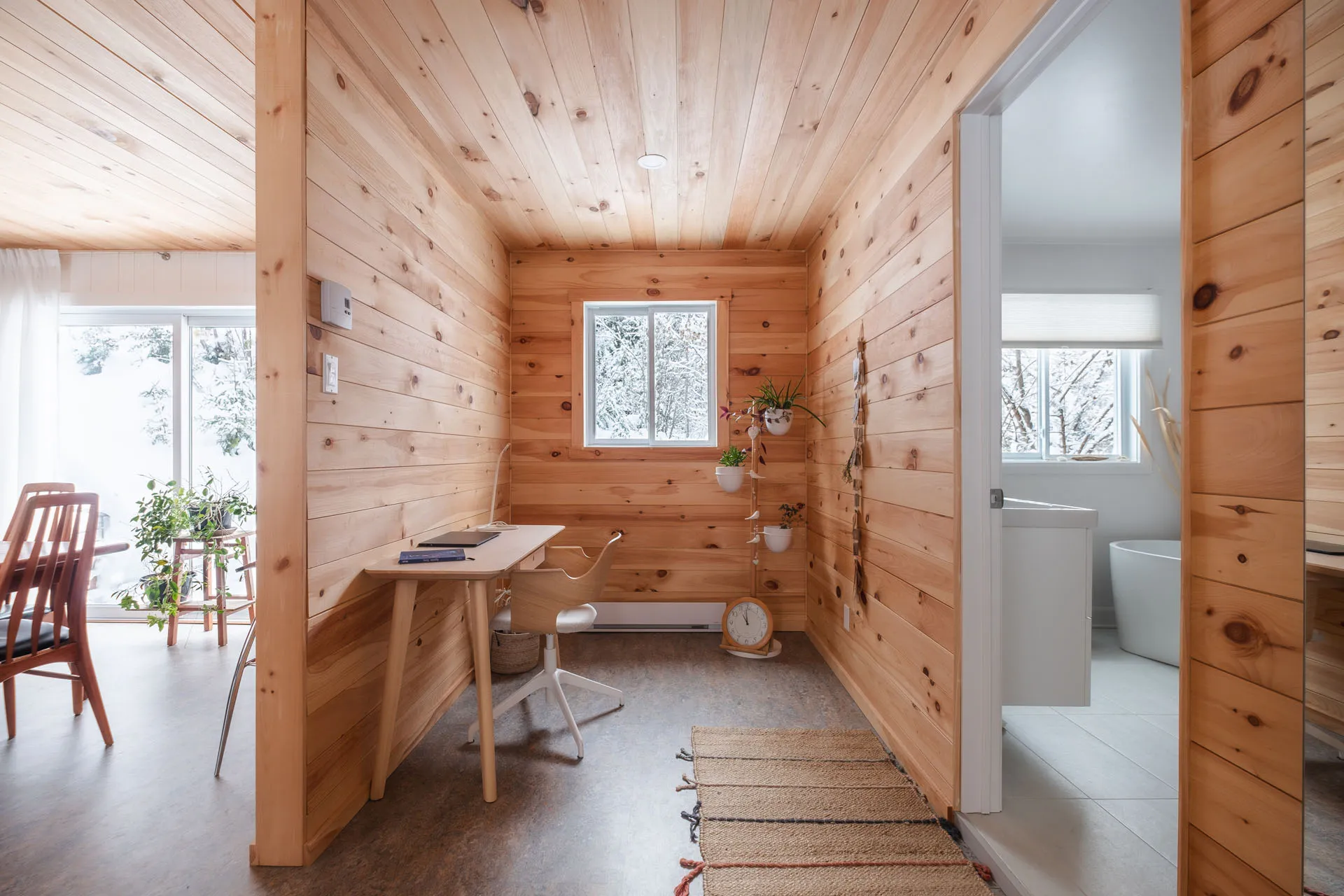 Solid wood desk in pine wood office with central window, white chair and hanging plants