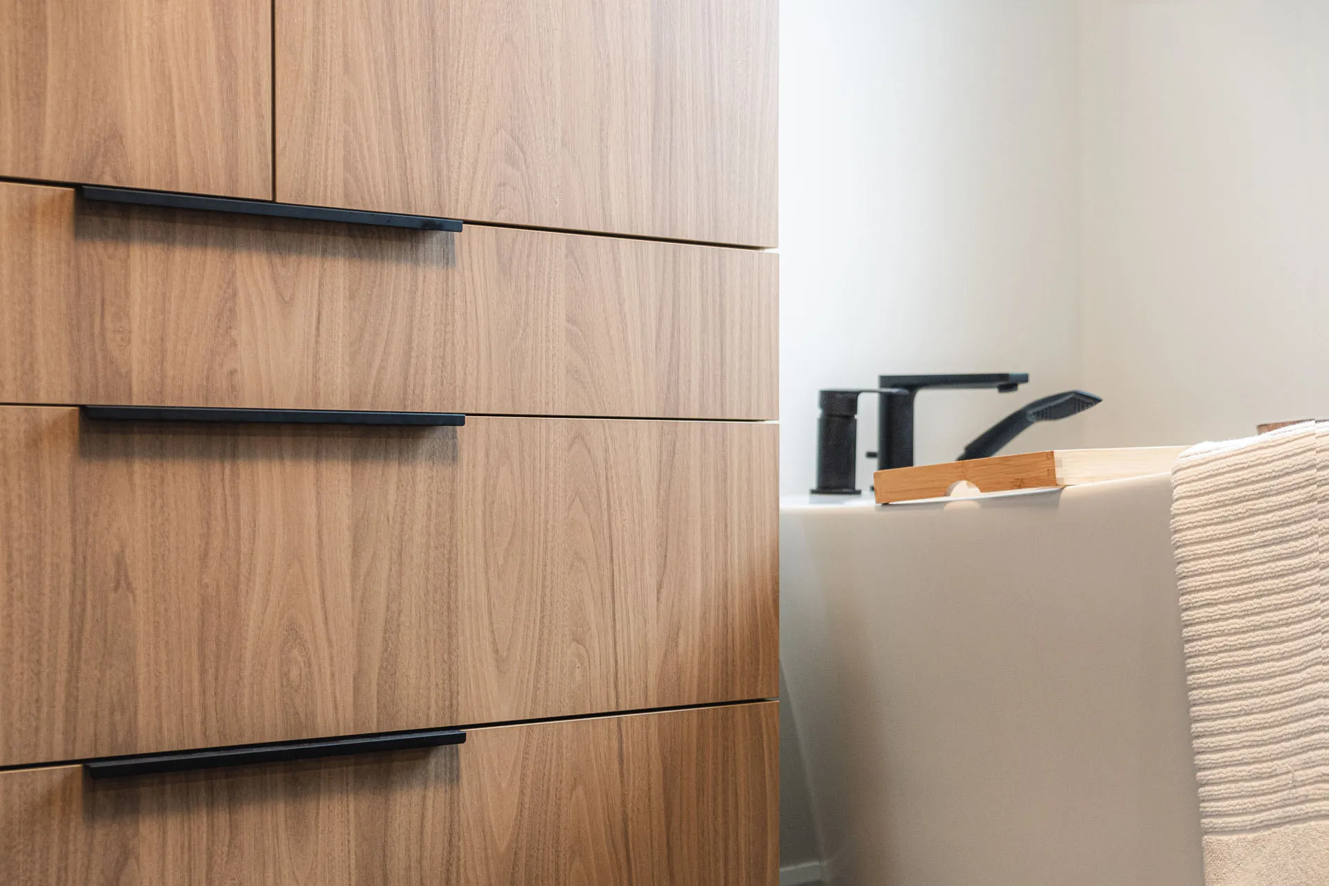 Natural wood bathroom cabinets with black handles, white countertop and modern faucet fixtures