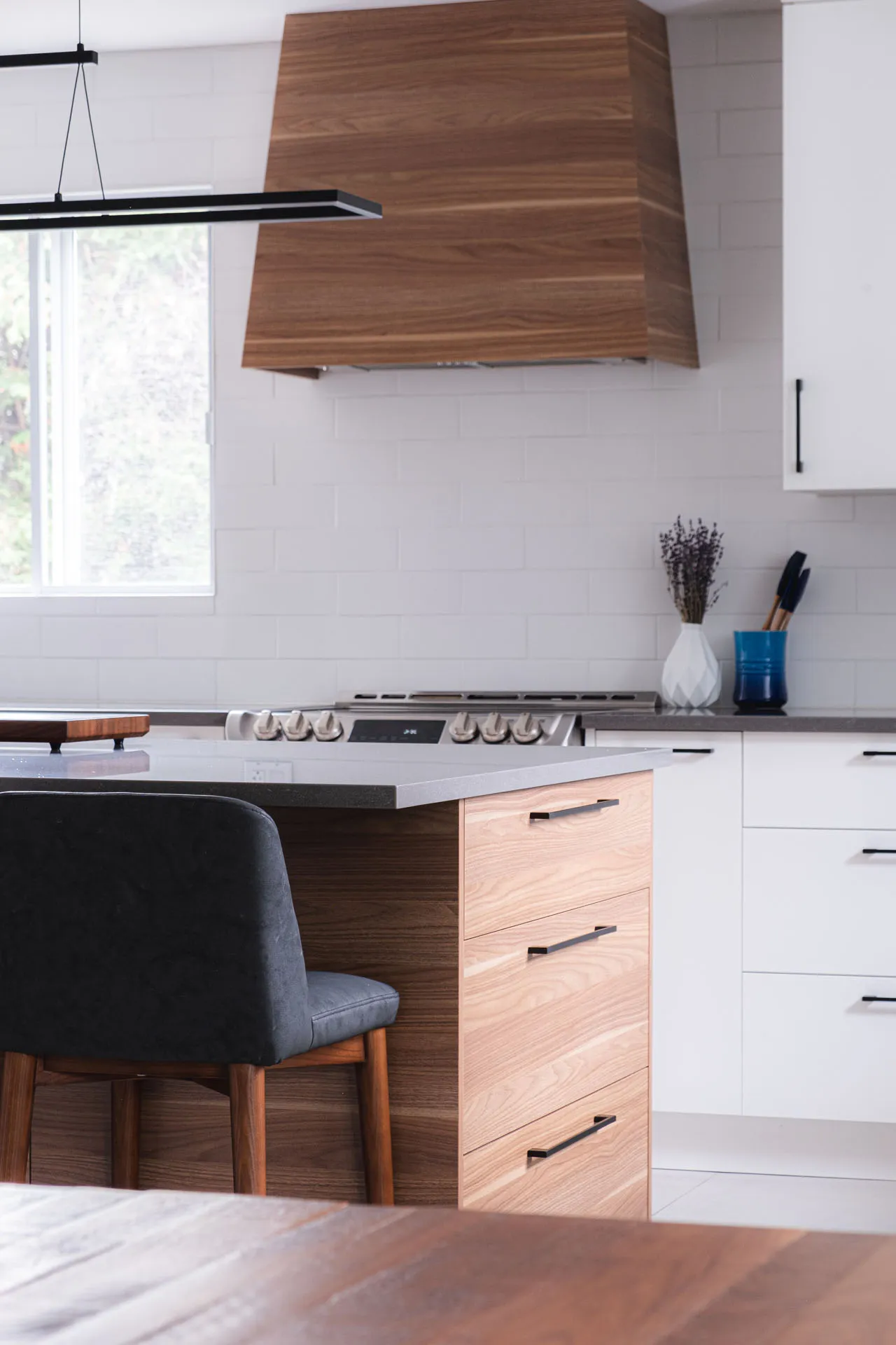 Modern Menuitech kitchen with white and wood cabinets, grey countertop, island with drawers, white subway backsplash, wood range hood