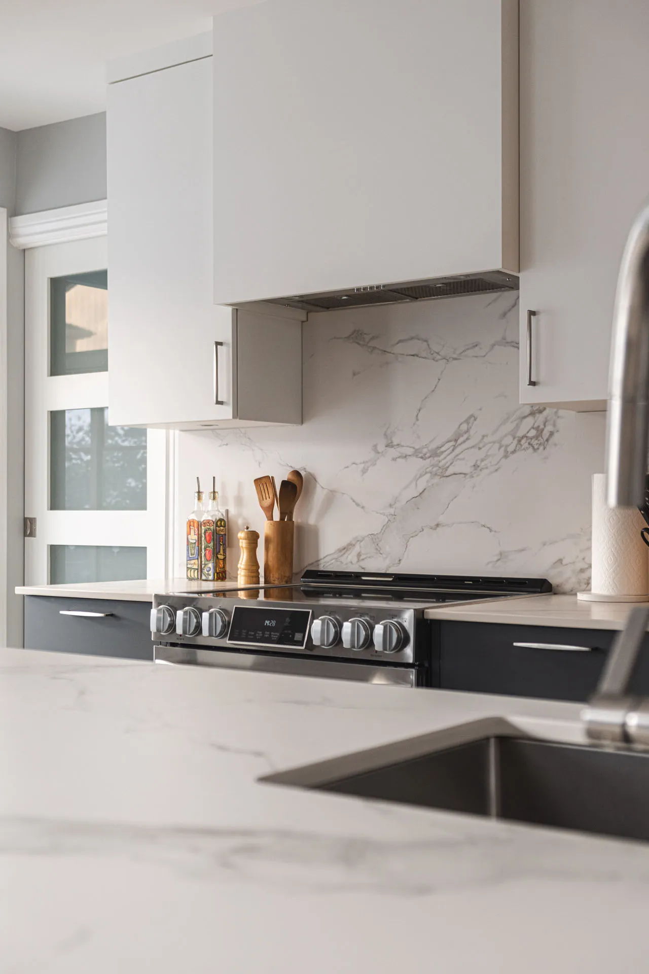 Modern Landry-D'Amours kitchen: white and grey cabinets, marble countertop, marble veining backsplash, white island, black range