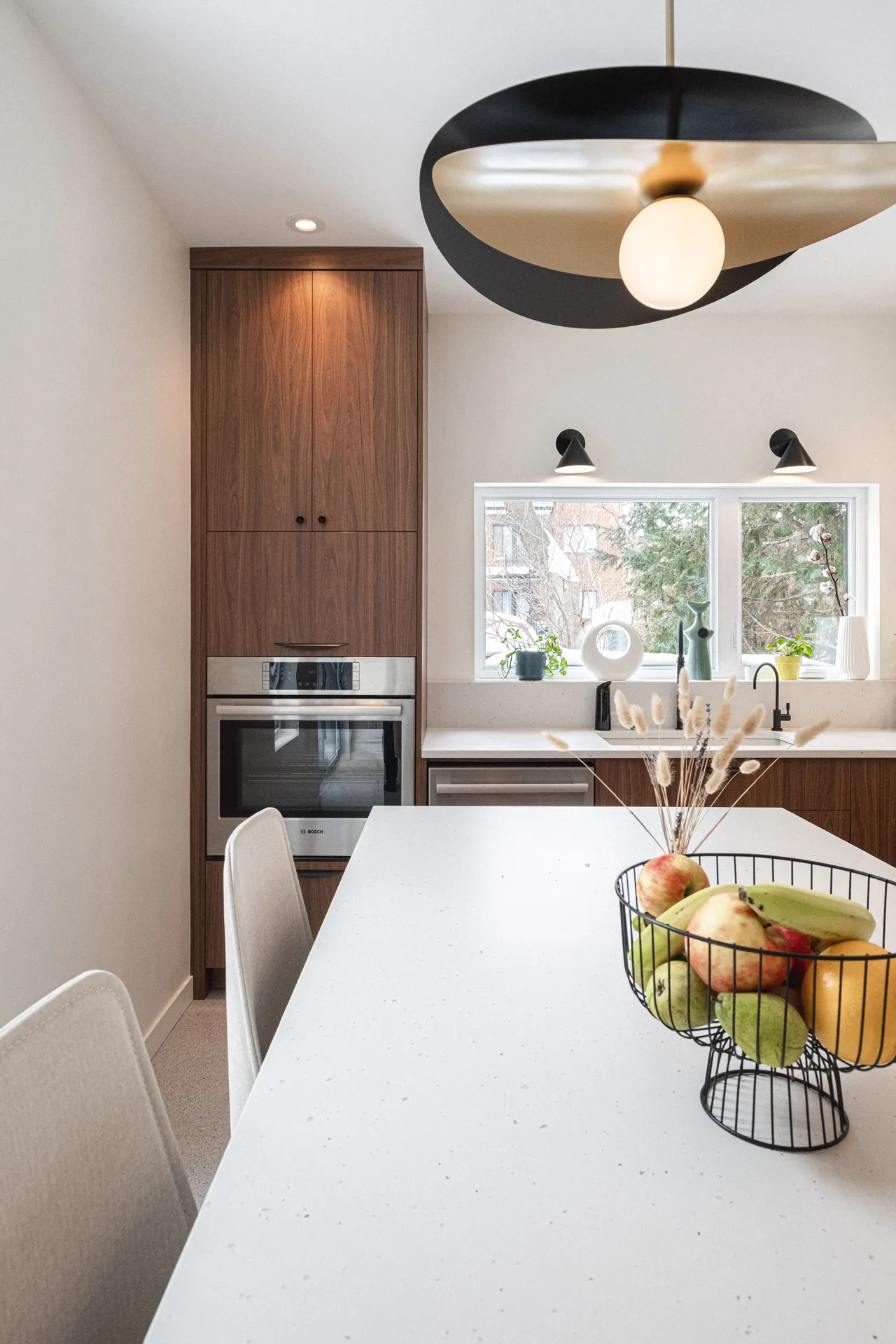 Cuisine moderne Menuitech Sudan avec armoires en noyer, comptoir blanc, îlot central et luminaire suspendu noir