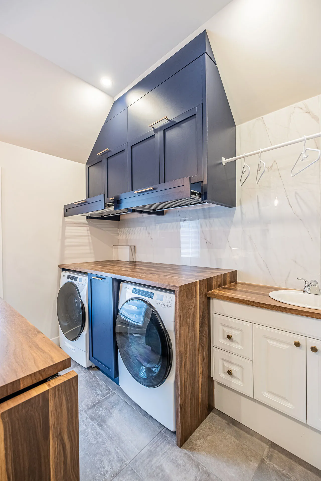 Modern laundry room with blue cabinetry, wooden countertop, integrated washers and white marble backsplash