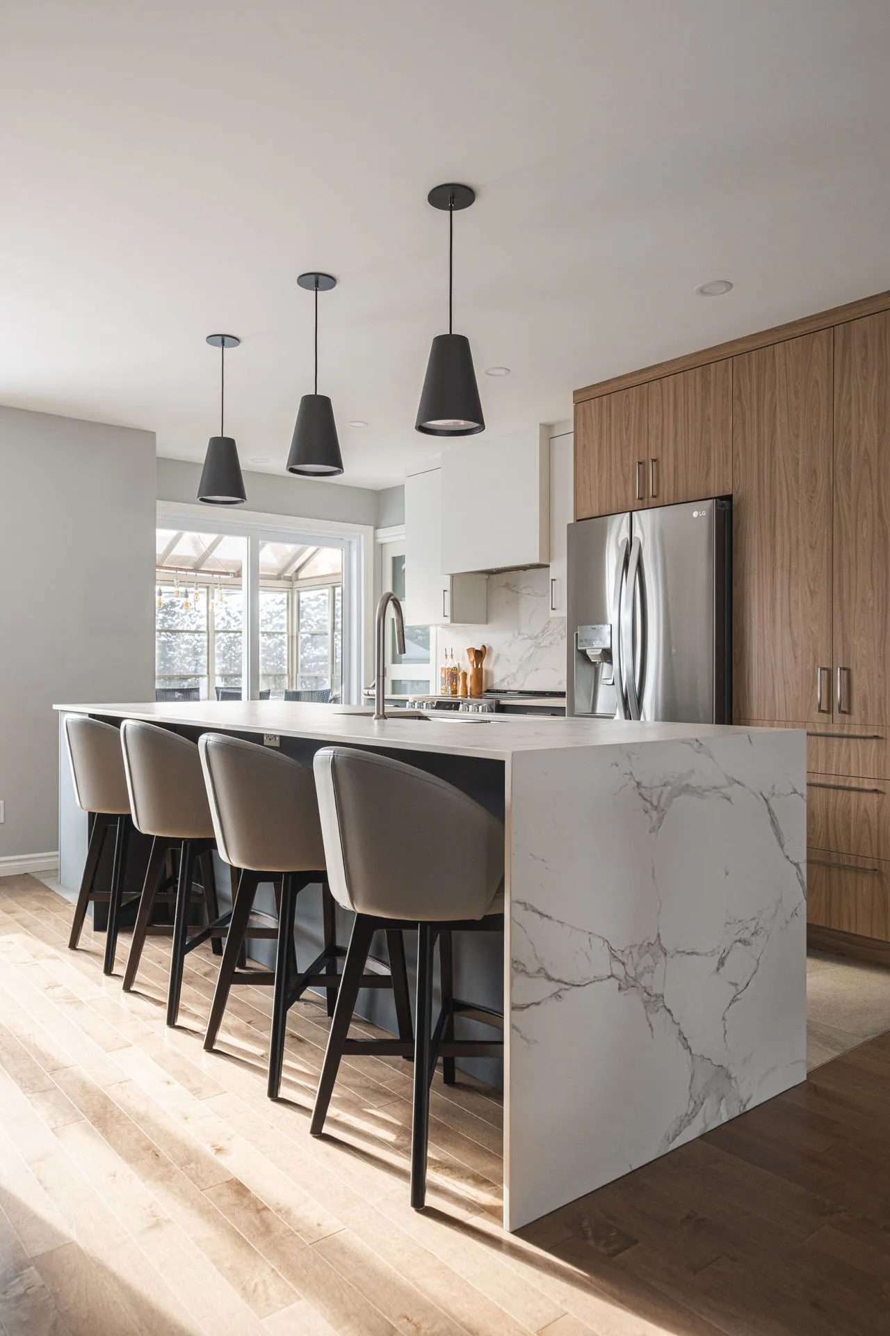 Modern Landry D'Amours kitchen: natural wood cabinets, white marble island, quartz countertop, black pendant lights, stainless steel appliances.