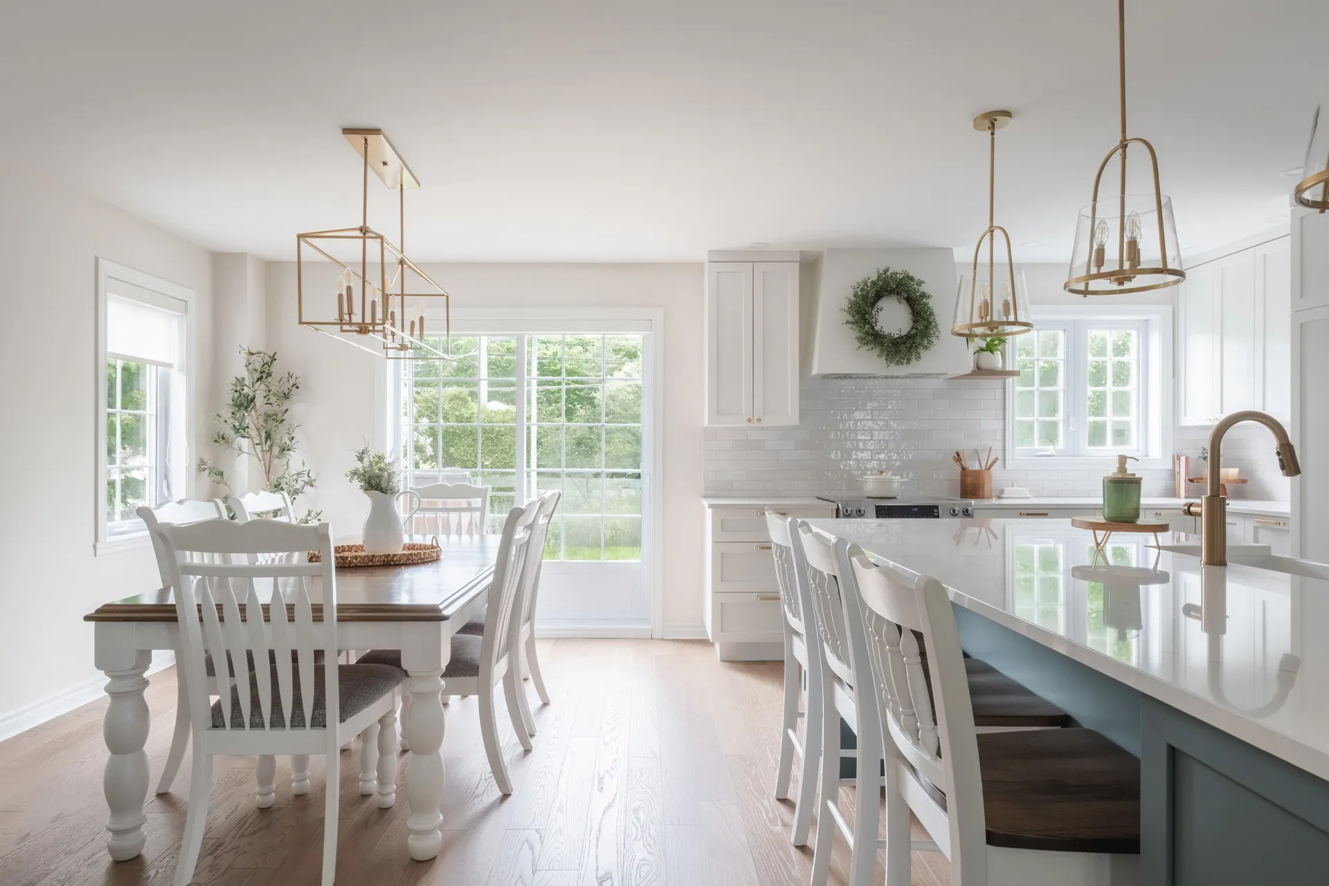 Modern white kitchen with blue-grey island, white countertop, subway tile backsplash, gold fixtures and large windows