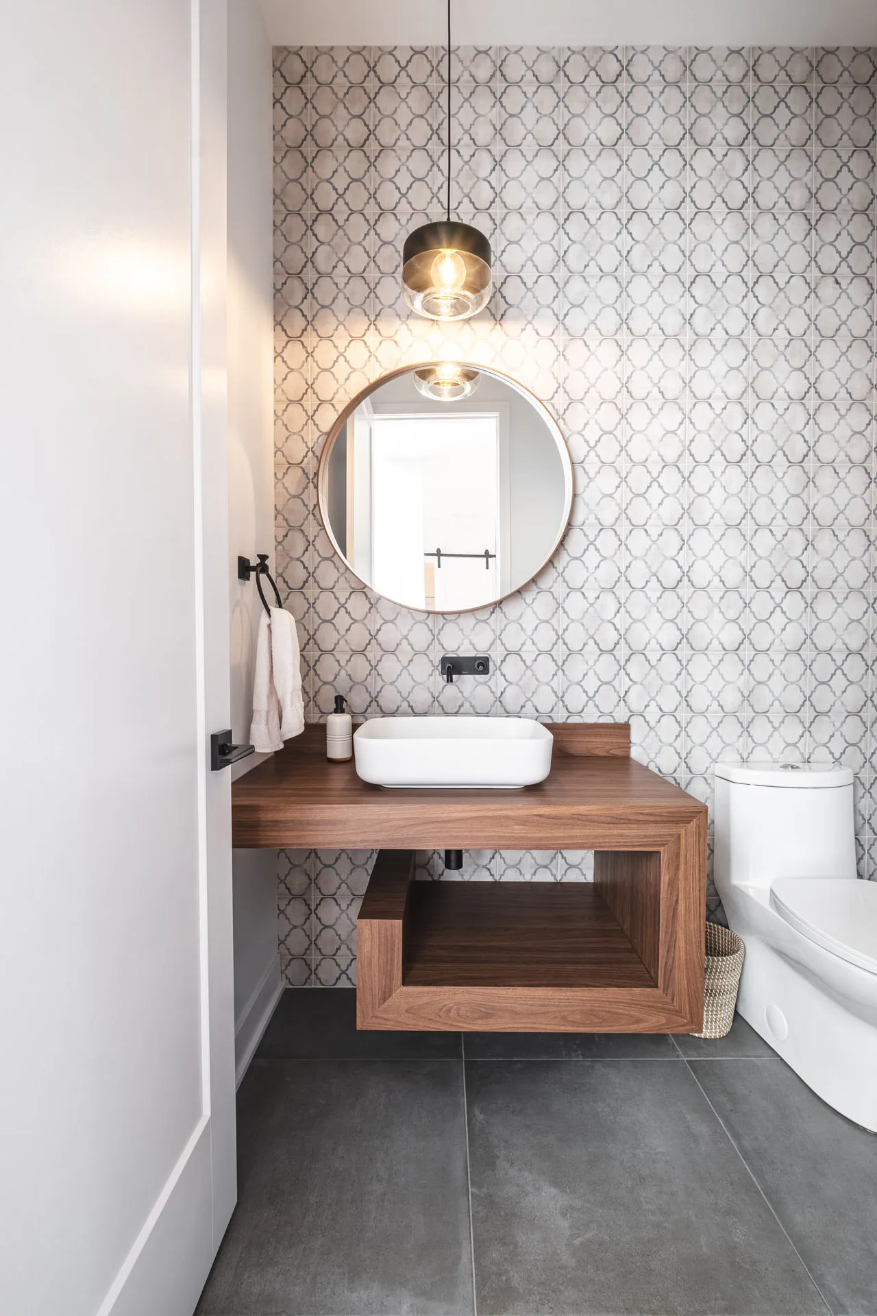 Diard bathroom: walnut wood vanity, wood countertop, gray geometric tile backsplash, round mirror, toilet