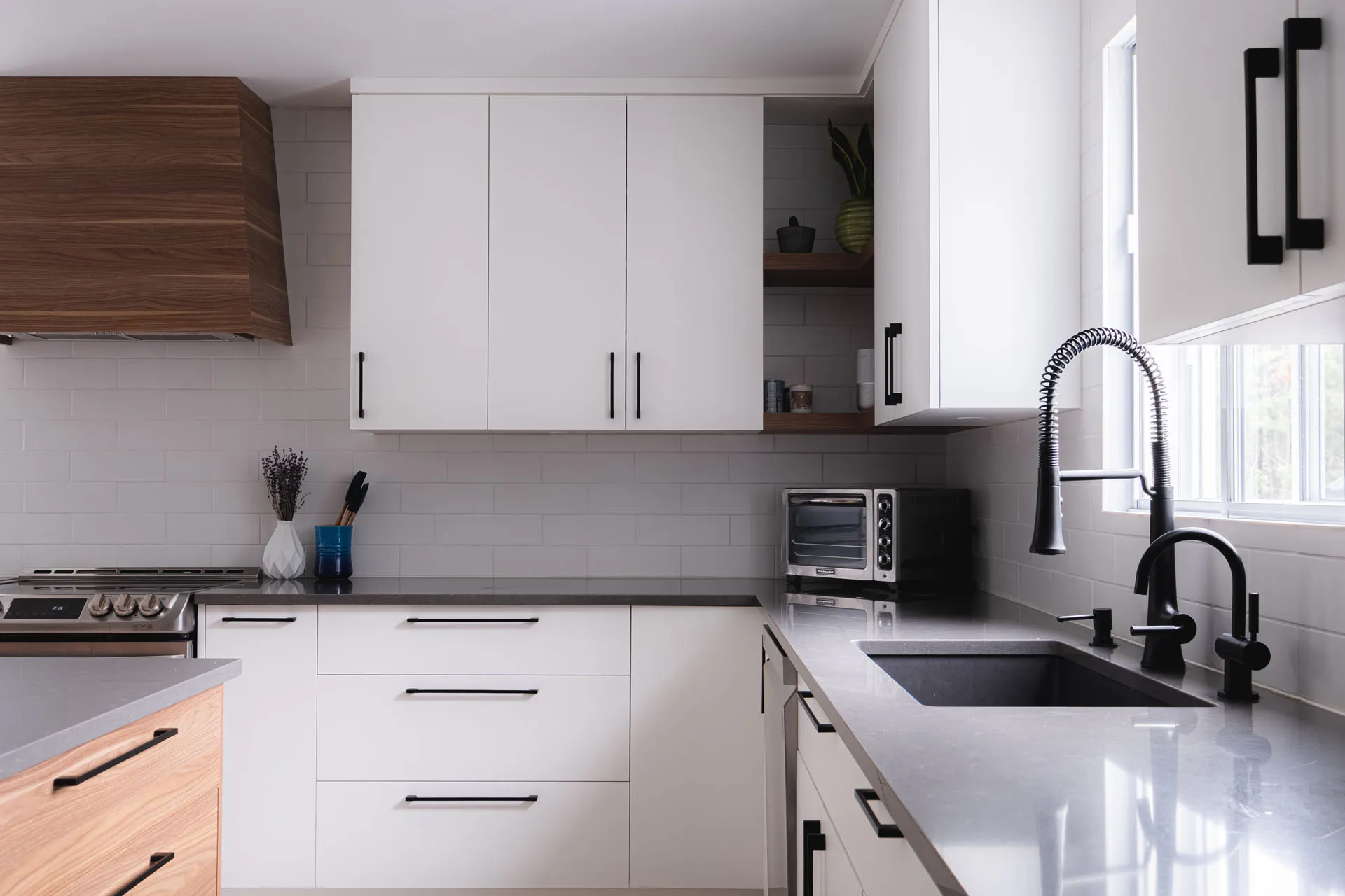 Modern Menuitech kitchen with white cabinets, grey countertop, white subway tile backsplash, black sink and integrated appliances