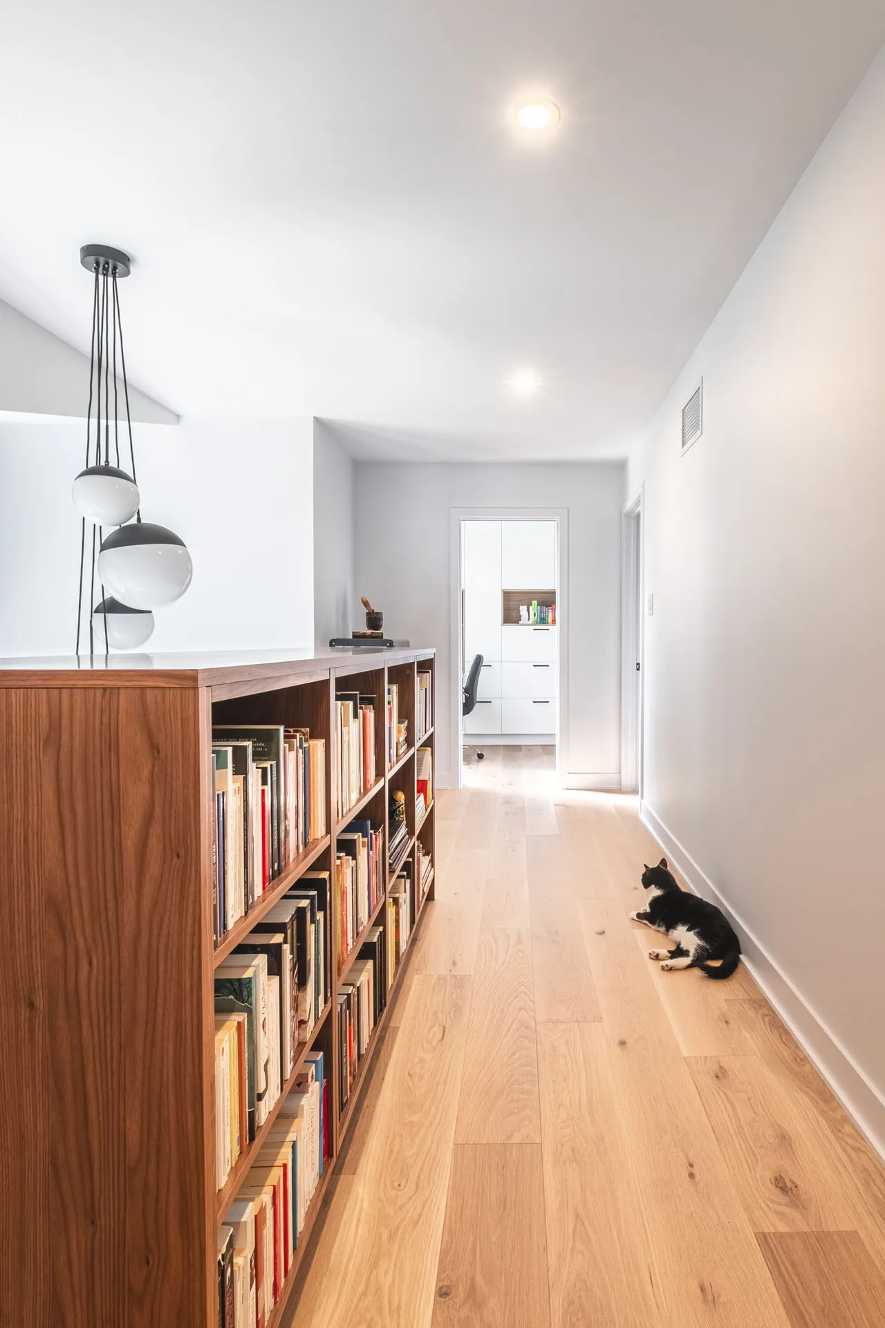 Modern hallway with wooden wall shelving unit, gray countertop, black pendant lights, light wood flooring