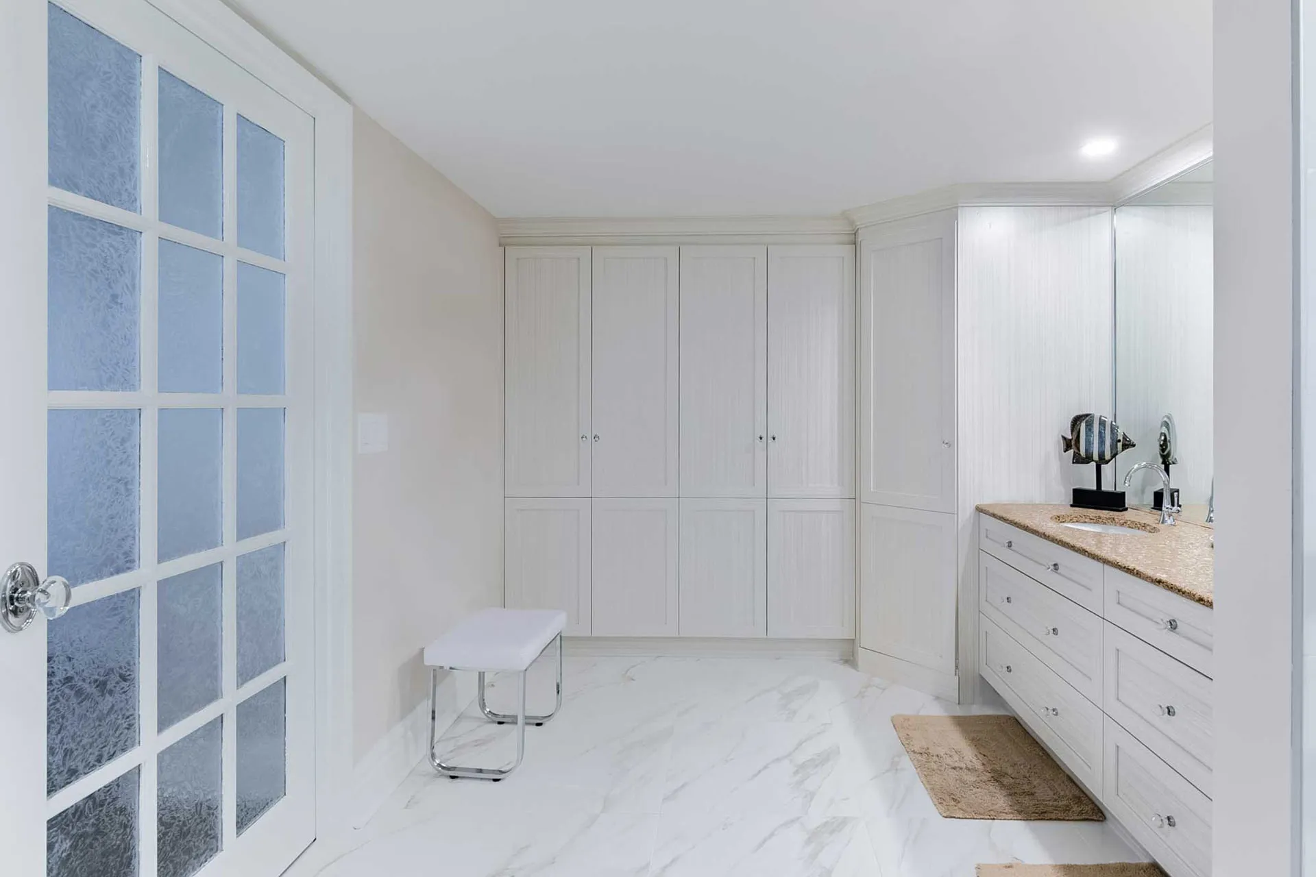 White bathroom with Menuitech cabinetry, beige granite countertop, framed mirror and white marble flooring