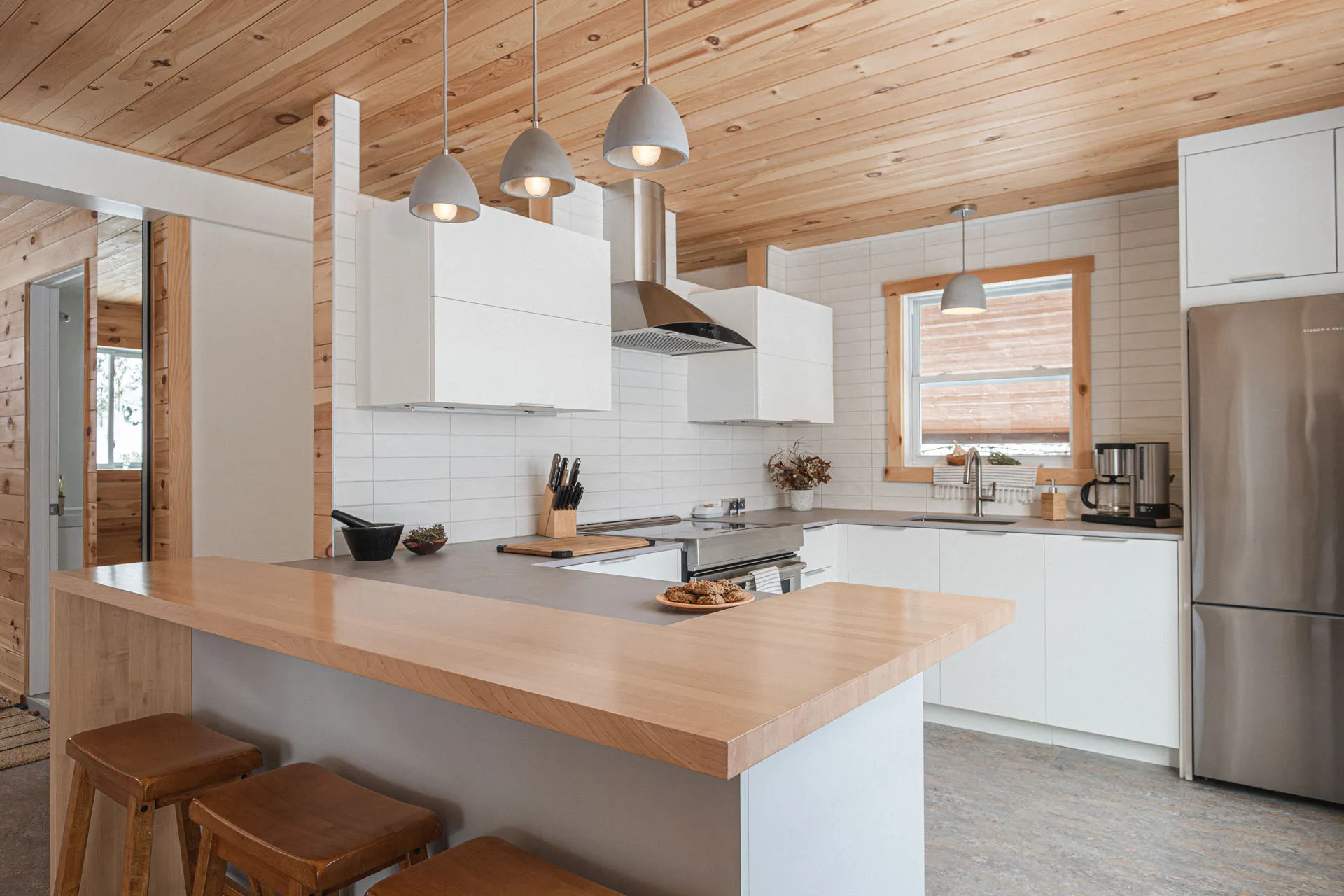 Valière kitchen: white cabinetry, light wood countertop, island with stools, subway tile backsplash, wood ceiling, pendant lights