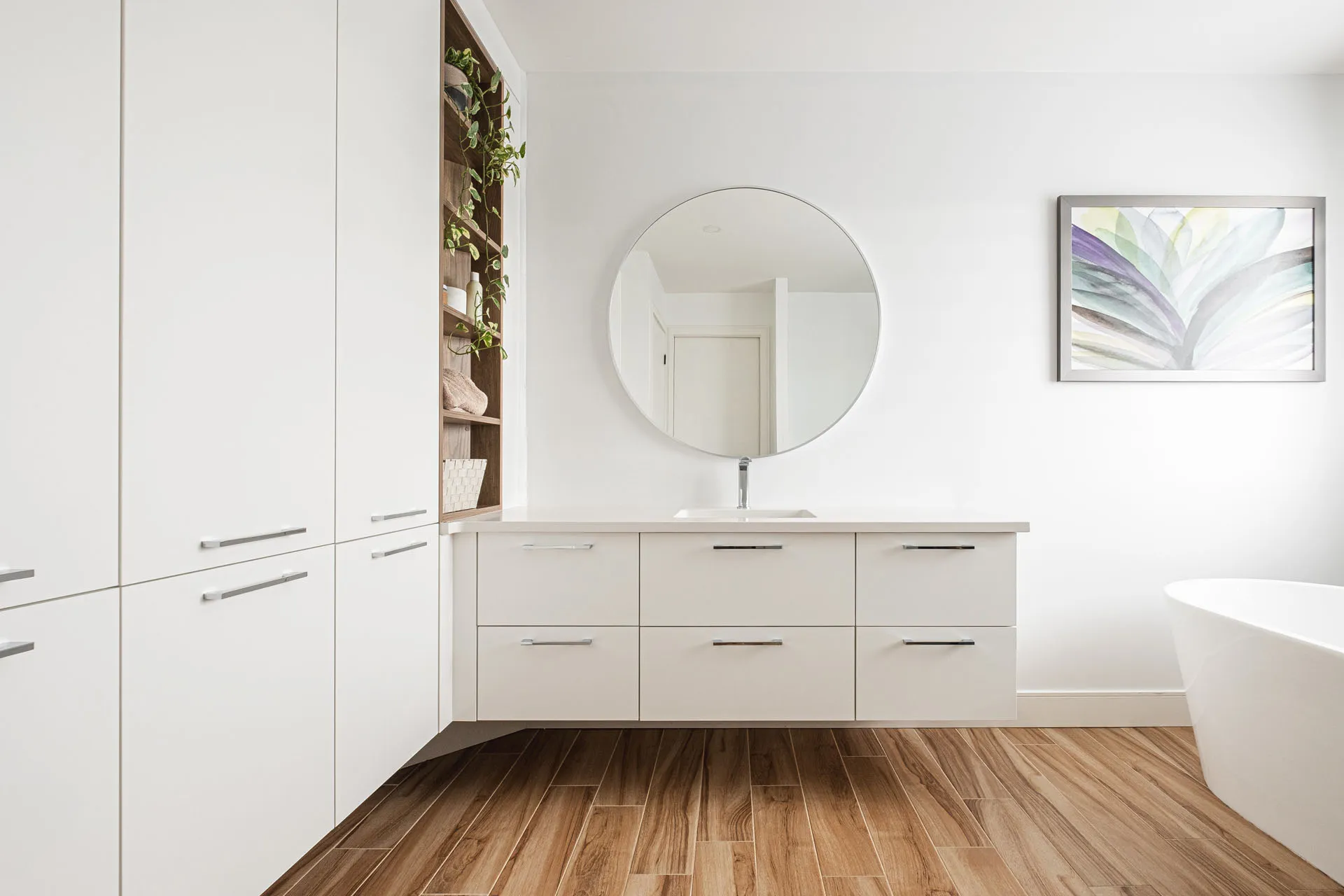 Modern bathroom with white lacquered cabinetry, light grey countertop, round mirror and wood flooring