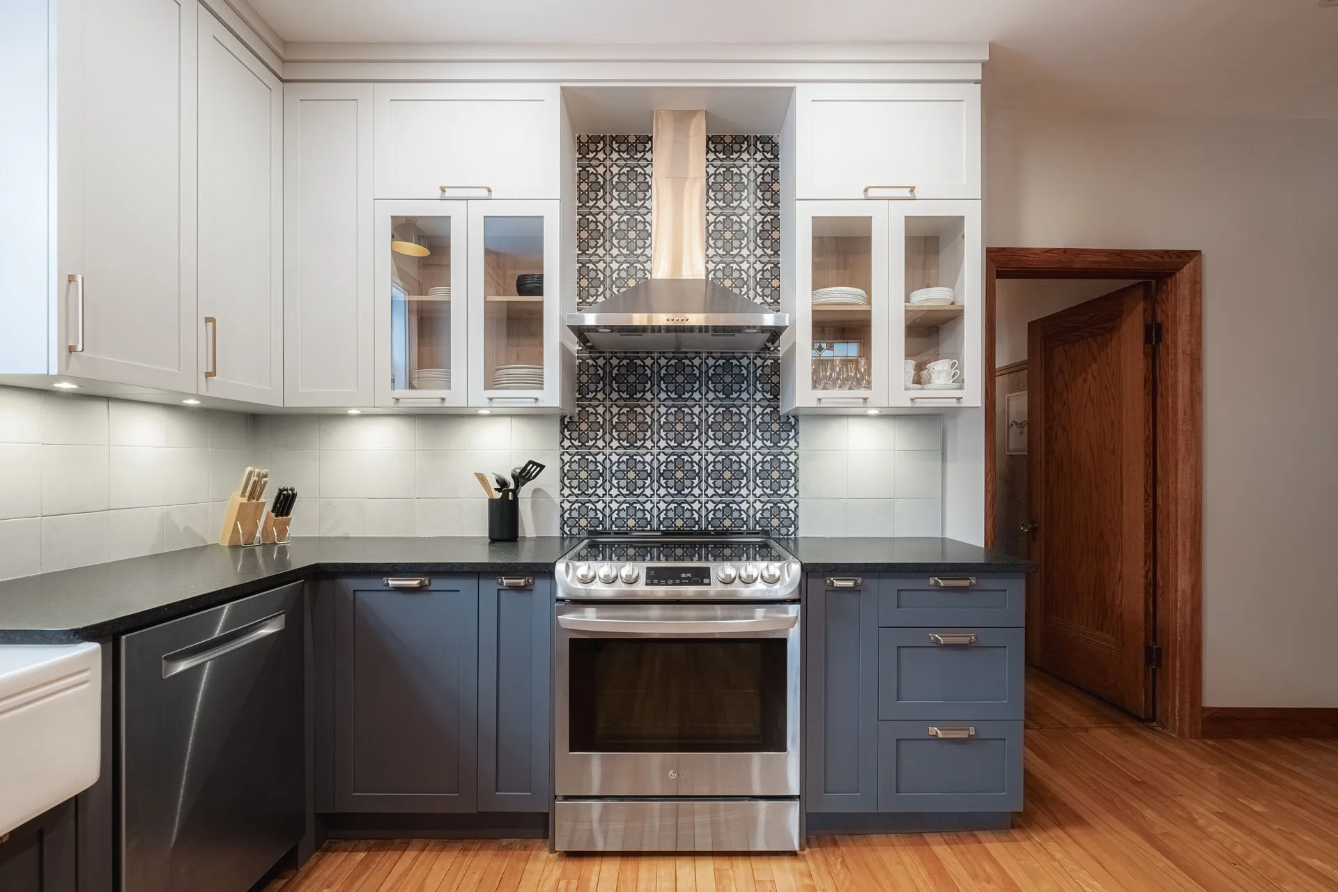 Modern Stephan kitchen: white and blue cabinets, black countertop, geometric tile backsplash, stainless steel range