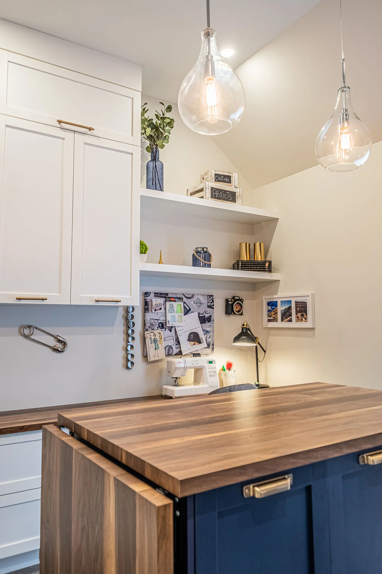 Modern kitchen with white cabinets, navy blue island, light wood countertop, grey backsplash and glass pendant lights
