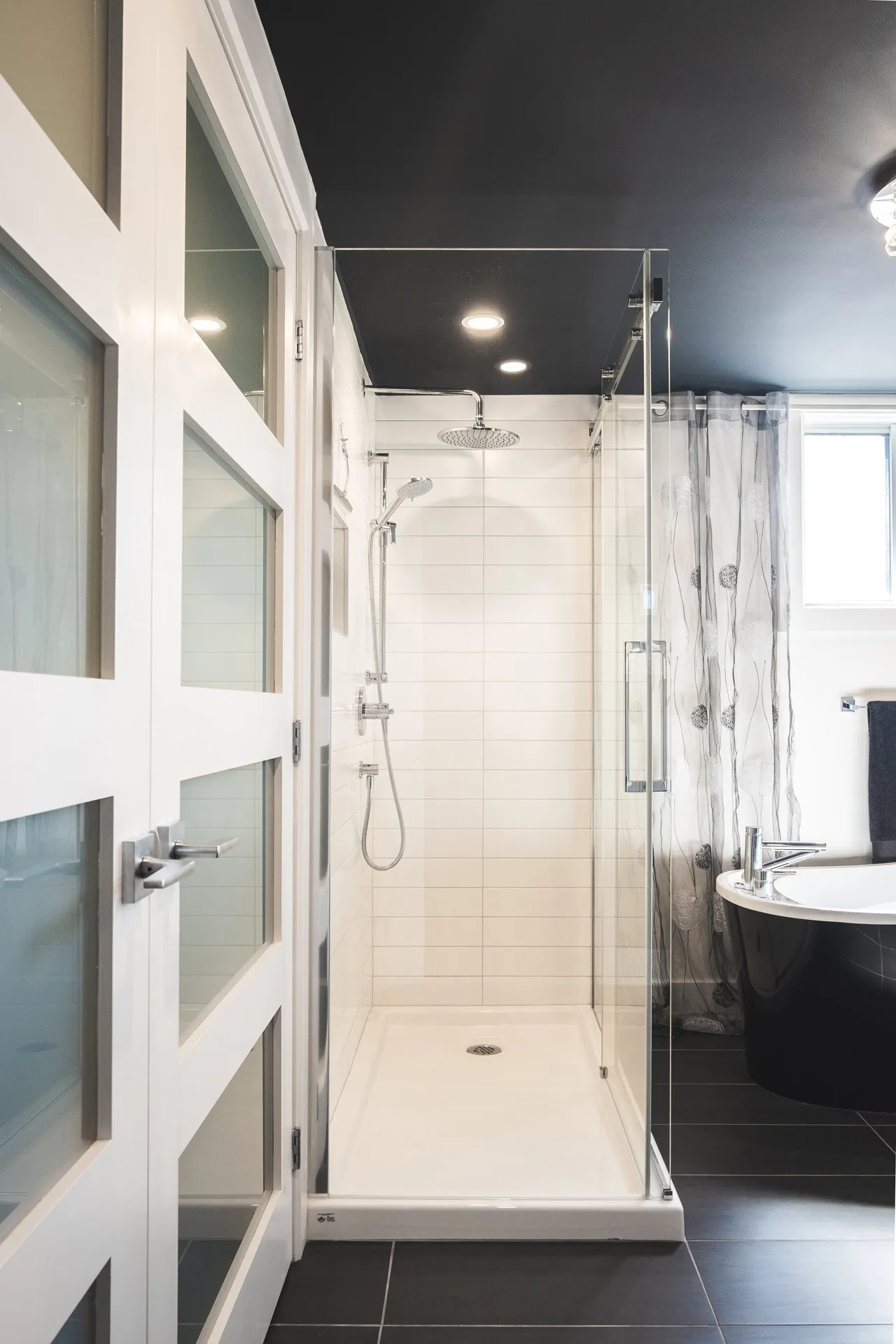 Modern Menuitech bathroom with glass shower enclosure, white cabinets, black countertop and grey tile