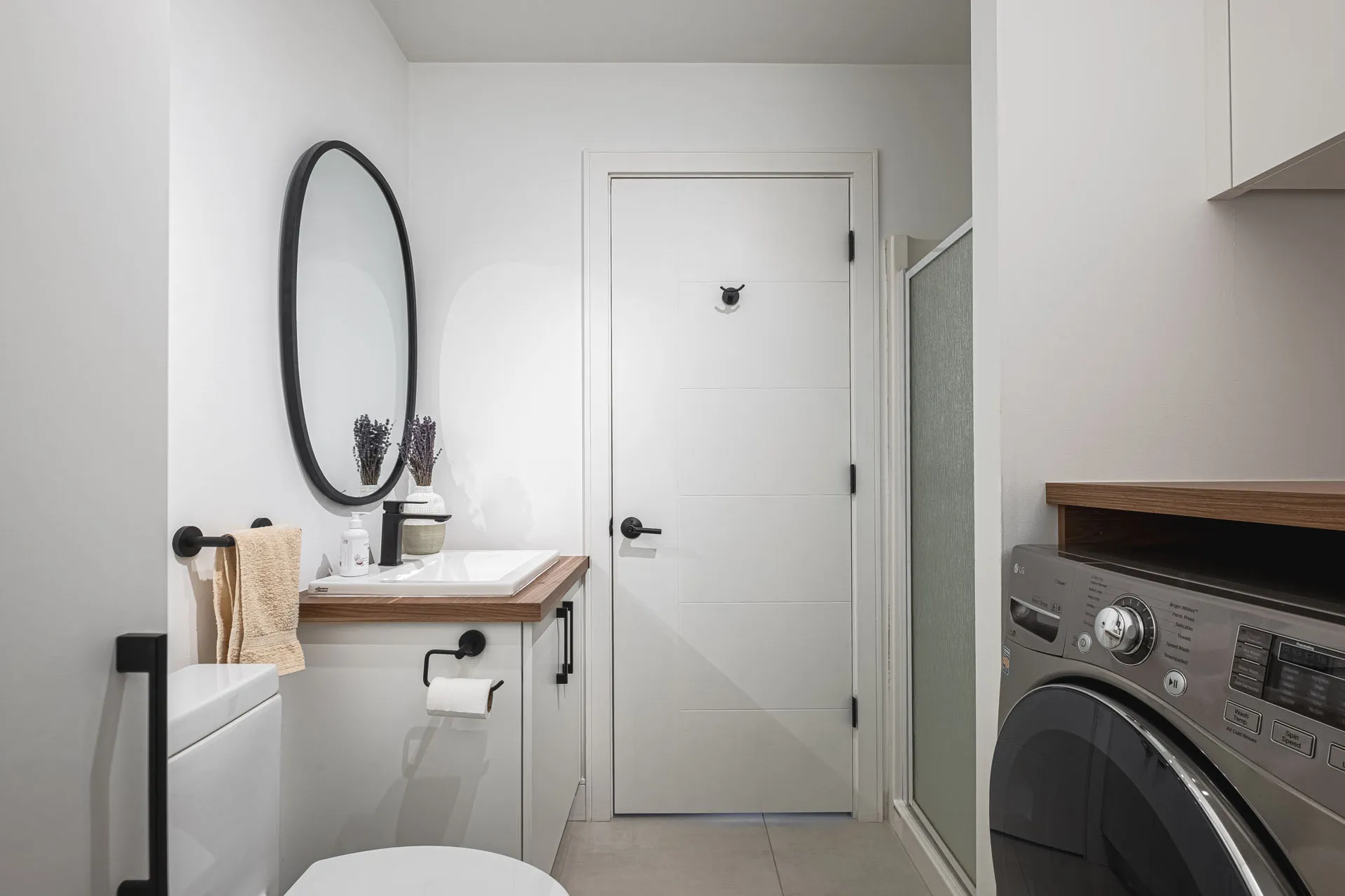 Modern bathroom with white cabinetry, wooden countertop, black oval mirror and integrated appliances