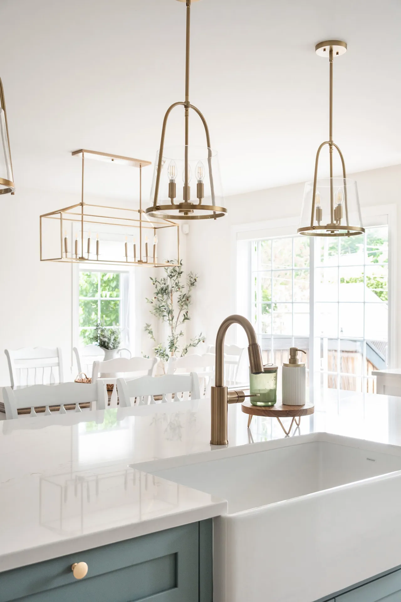 Modern kitchen with sage green island, white countertops, brass fixtures and panoramic windows
