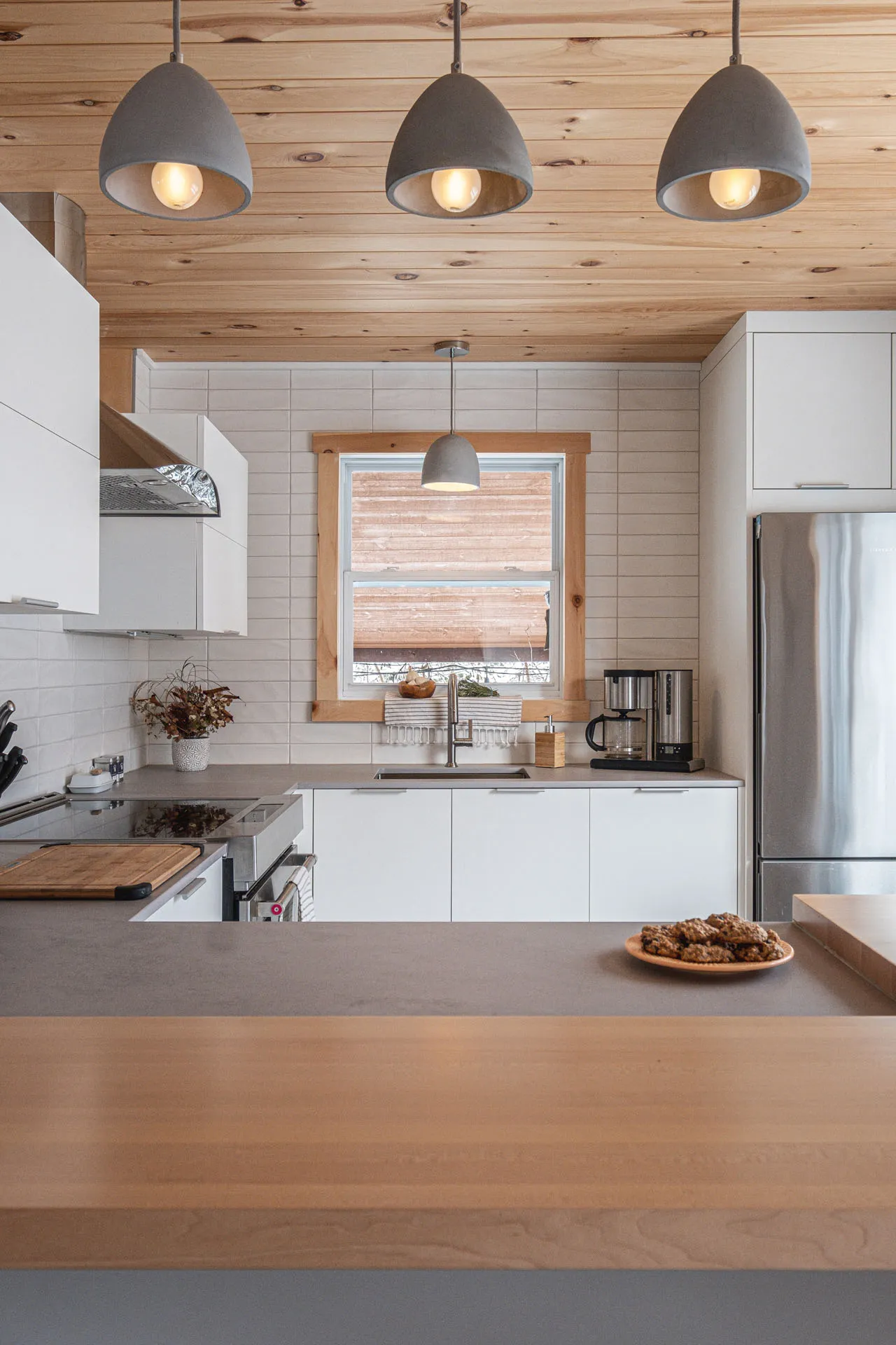 Menuitech Valière kitchen: white cabinetry, grey countertop, wood island, white subway tile backsplash, wood ceiling, grey pendant lights.