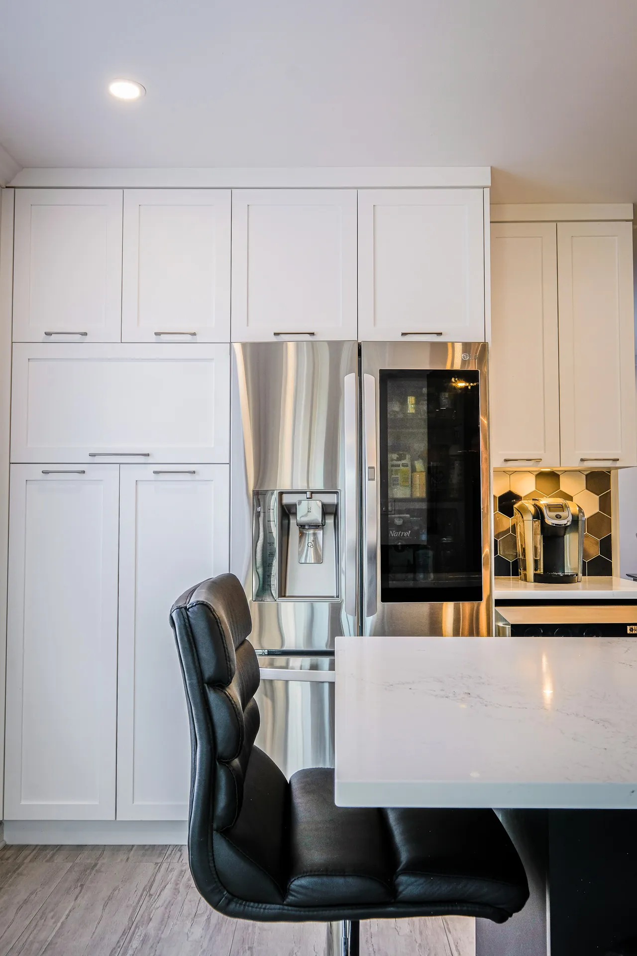 Modern Landry kitchen: white cabinetry, marble countertop, island, stainless steel refrigerator, geometric gold backsplash