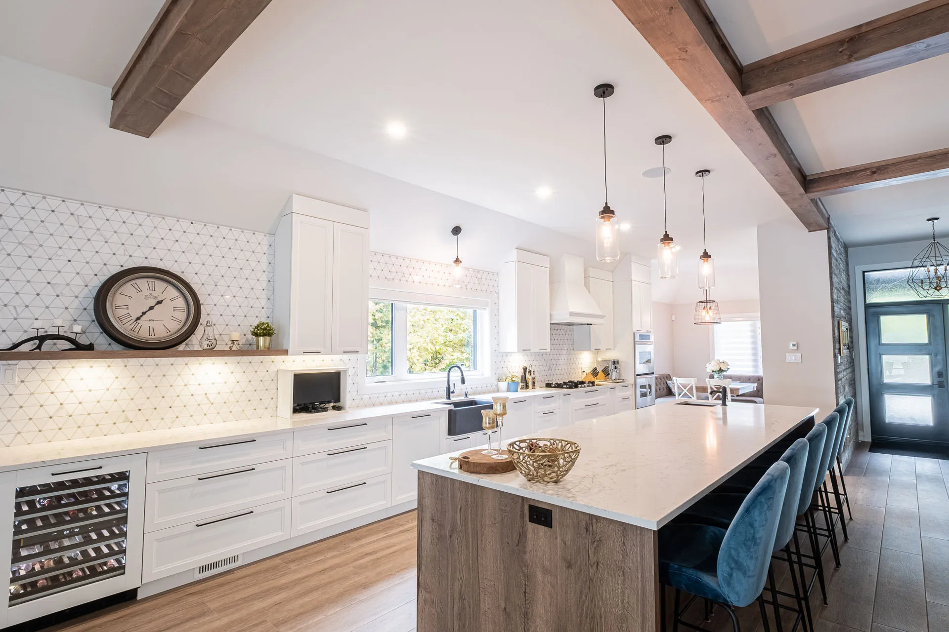Modern white kitchen with wooden island, marble countertop, geometric backsplash, exposed beams and pendant lights