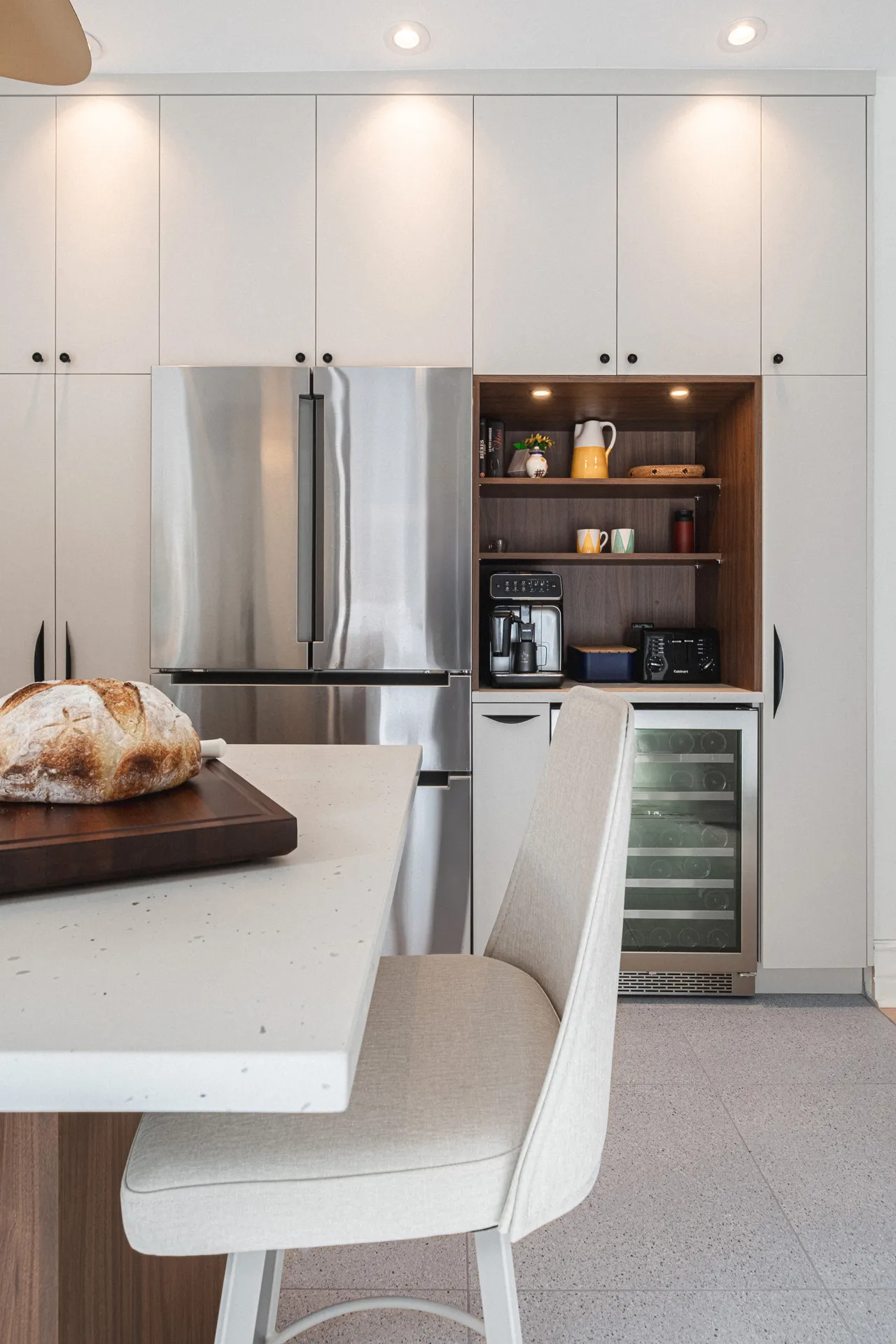 Cuisine moderne Menuitech Sudan : armoires blanches, comptoir quartz, îlot bois, niche bois foncé, réfrigérateur acier inoxydable