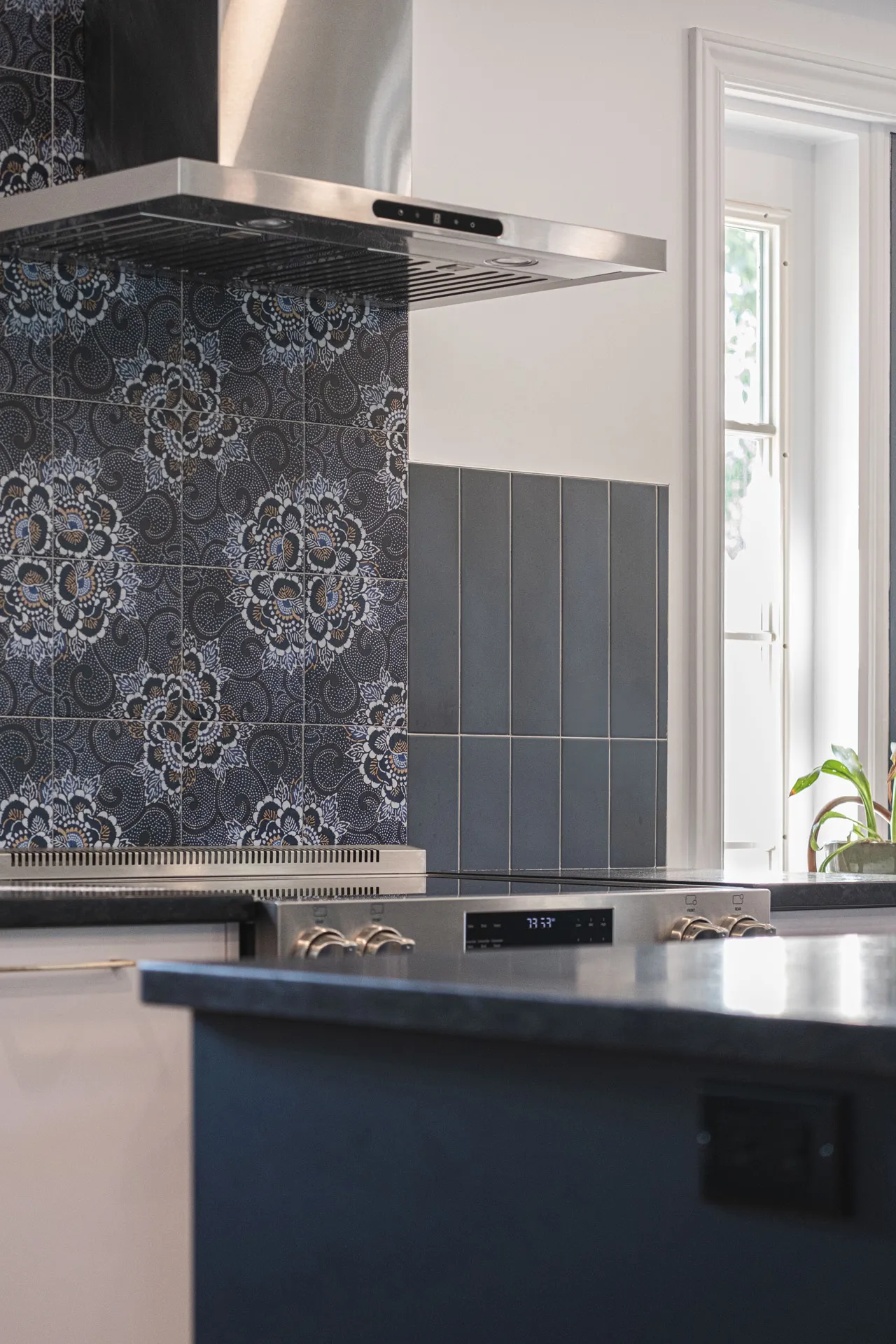 Modern Montreal kitchen: slate blue cabinets, black countertop, lace tile backsplash, stainless hood, island