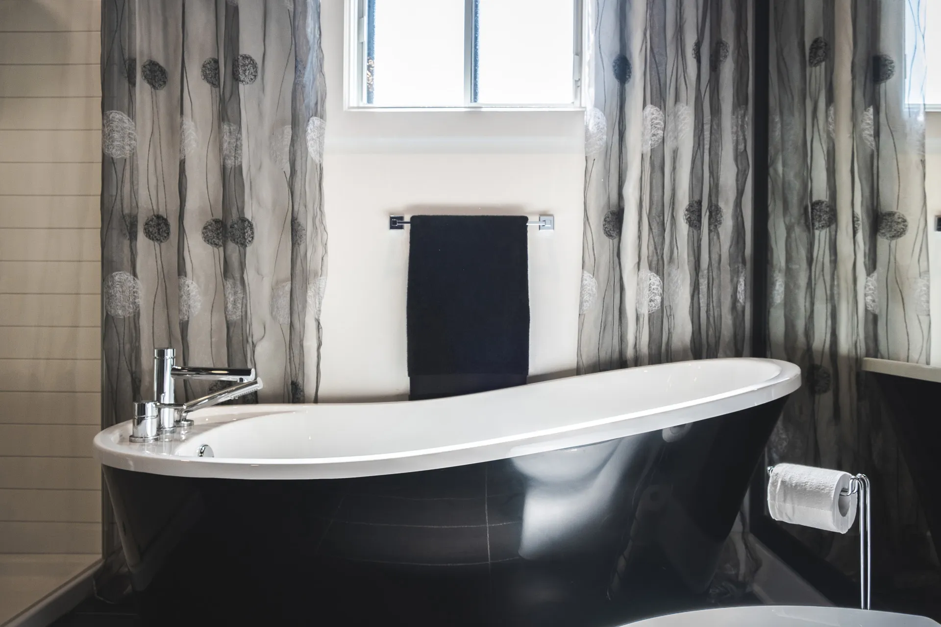 Modern Pagé bathroom featuring black freestanding tub, white countertop, beige tile and gray dandelion-patterned curtains
