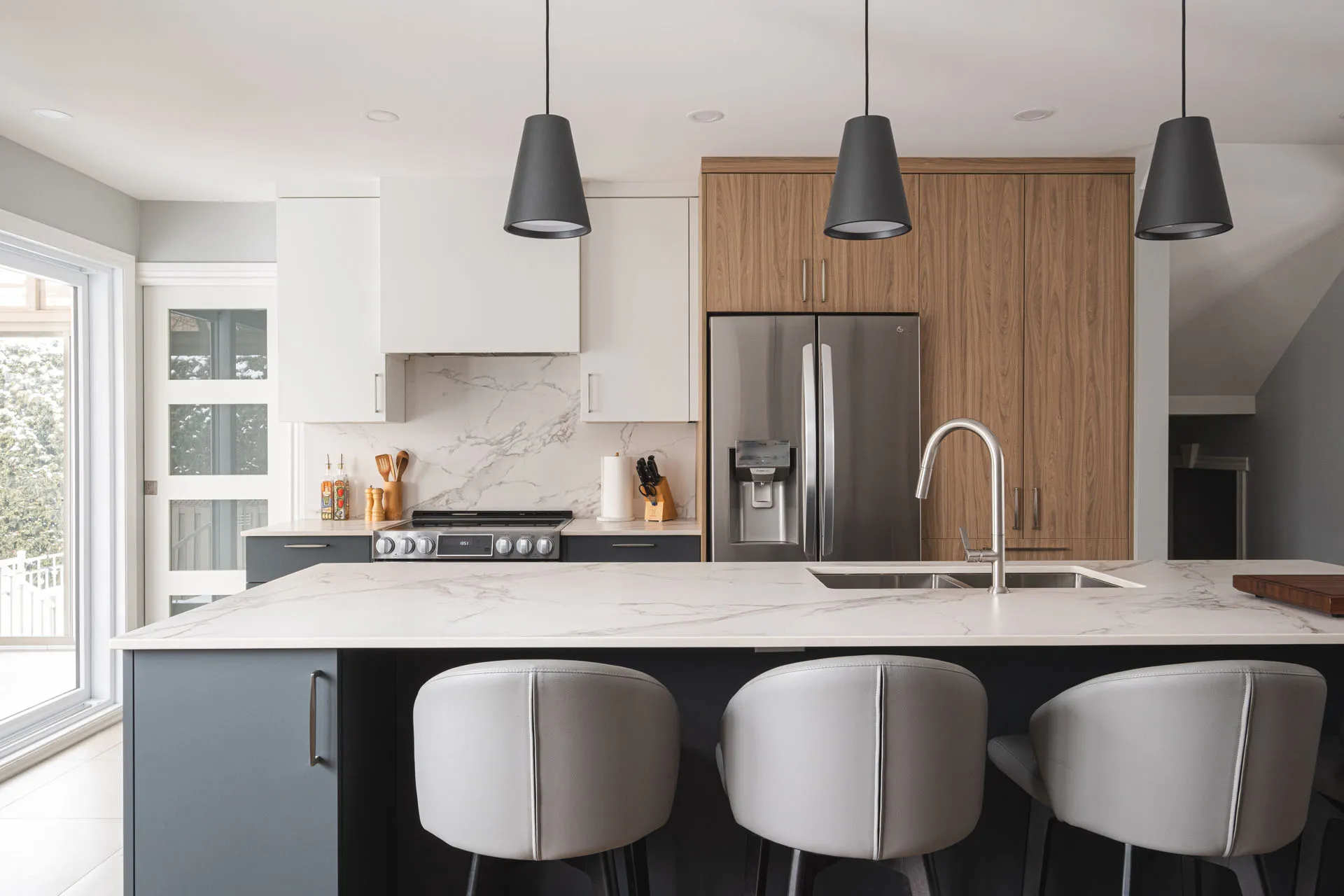 Modern Boisbriand kitchen: white and wood cabinets, black island, marble countertop, black pendant lights, stainless steel