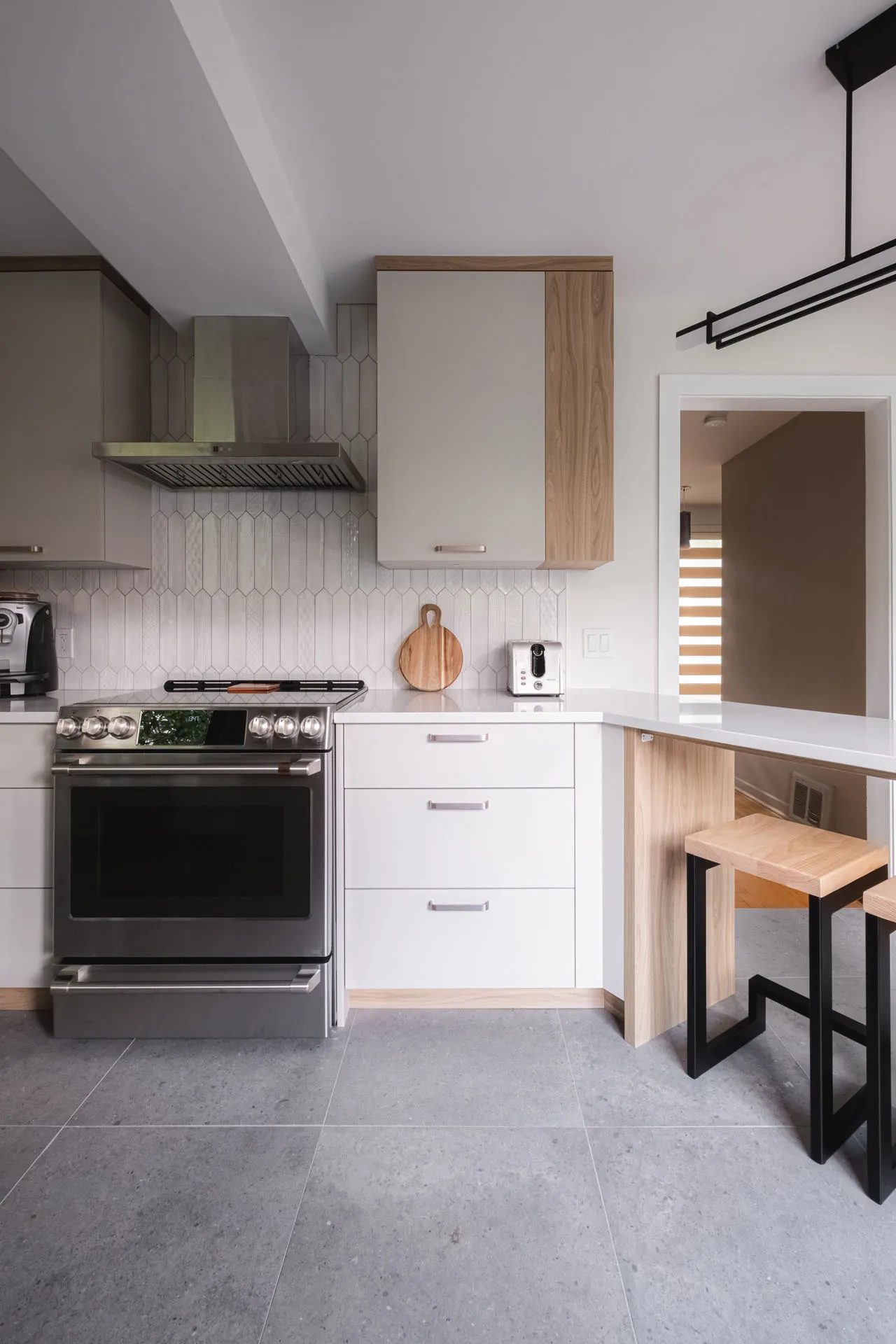 Modern white and wood kitchen with custom cabinetry, grey countertop, island, white tile backsplash, black range