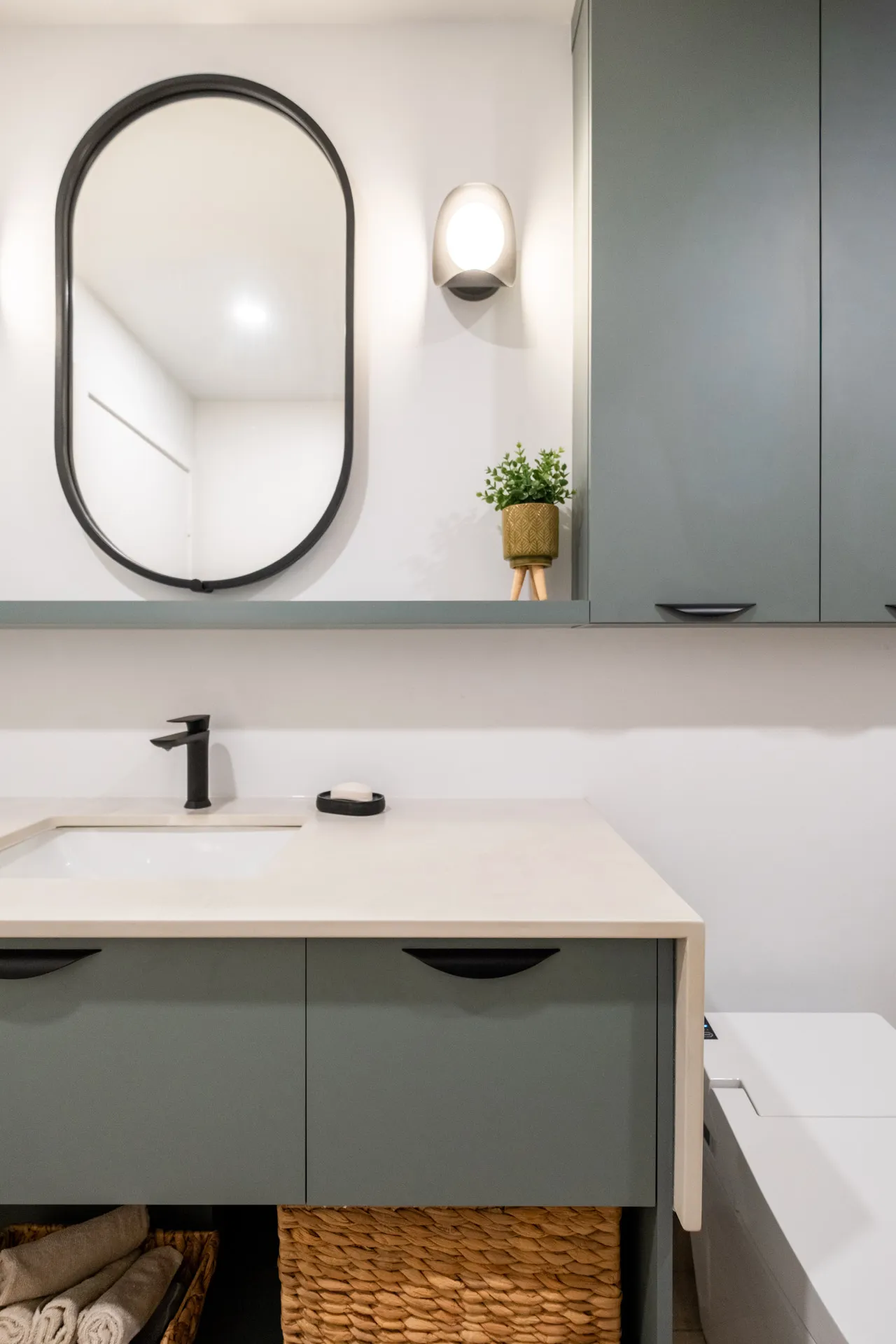 Salle de bain Fabiola : vanité grise avec comptoir blanc, miroir ovale noir, applique murale et baignoire