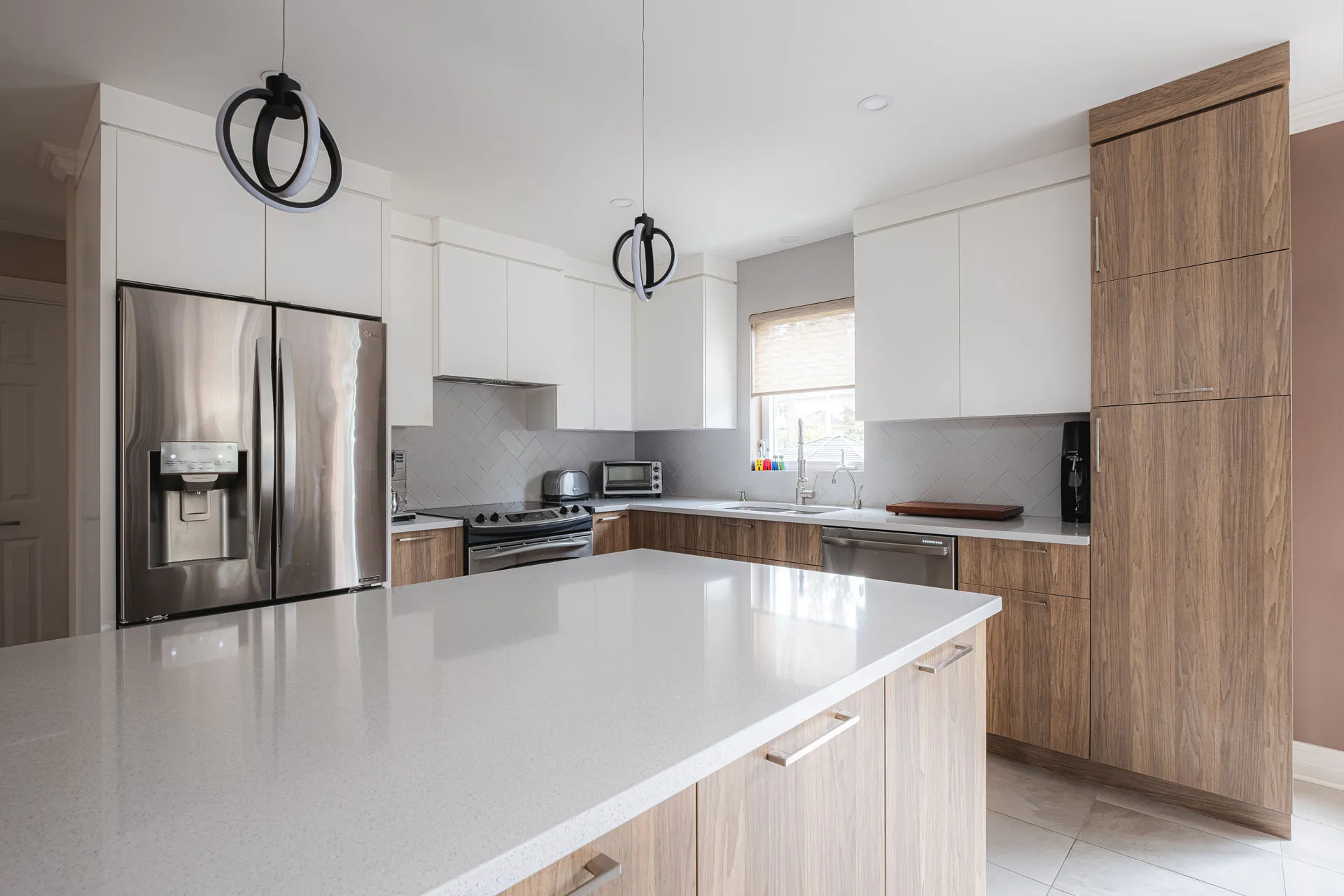 Menuitech kitchen with white and wood cabinets, white countertop, island, herringbone tile backsplash, black pendant lights