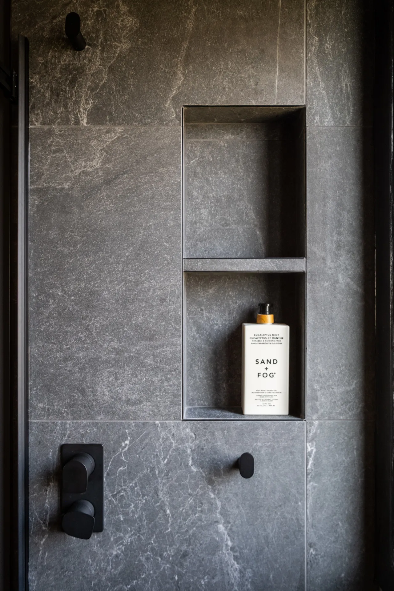 Salle de bain moderne avec niche murale en marbre gris, robinetterie noire et accessoires de rangement intégrés