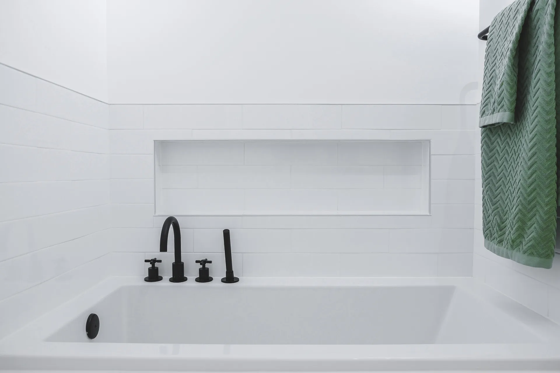 Modern bathroom with white soaking tub, white subway tile backsplash, matte black faucet and green textured towel