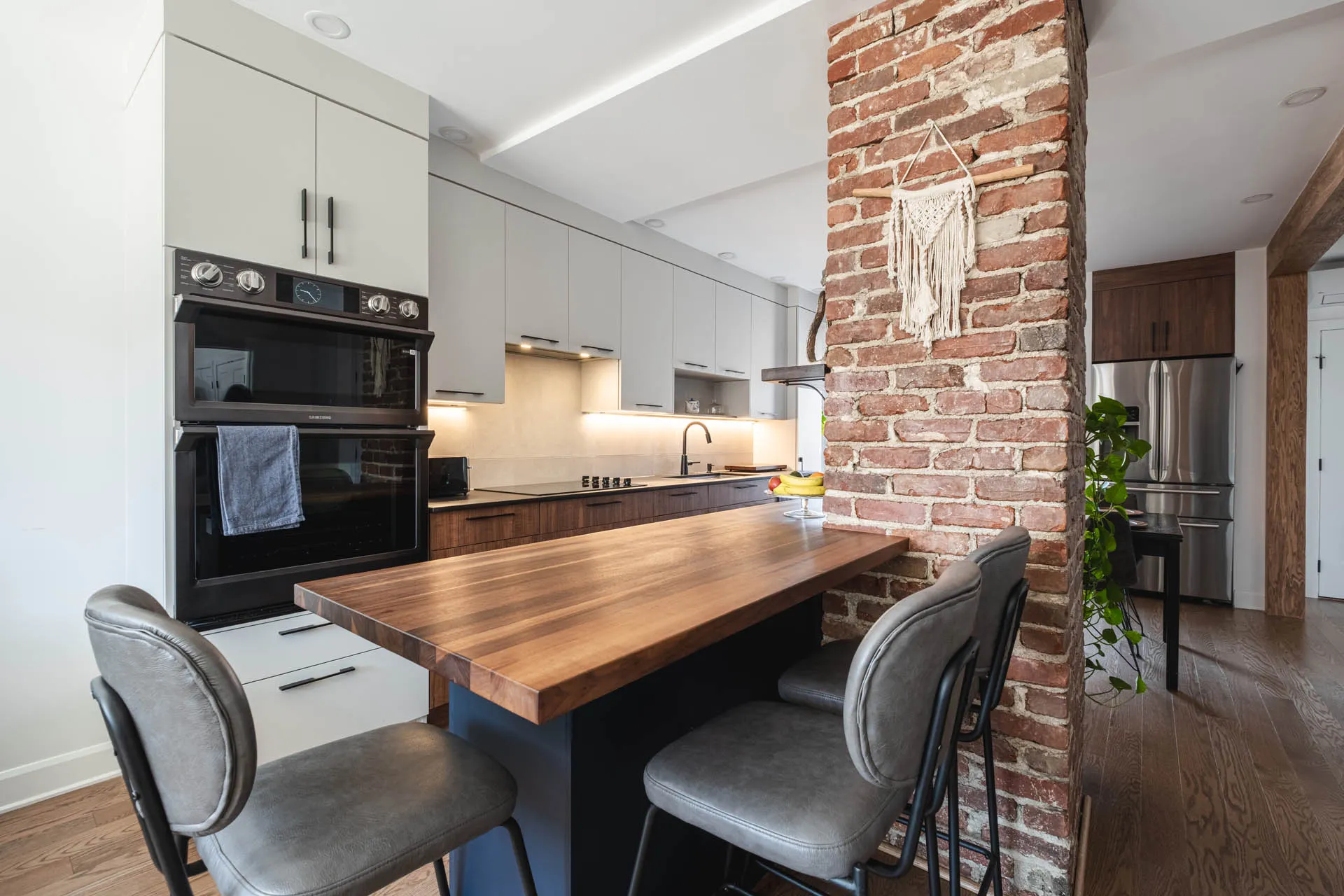 Florez Kitchen Montreal: grey and walnut cabinets, wood countertop, navy island, white backsplash, exposed brick