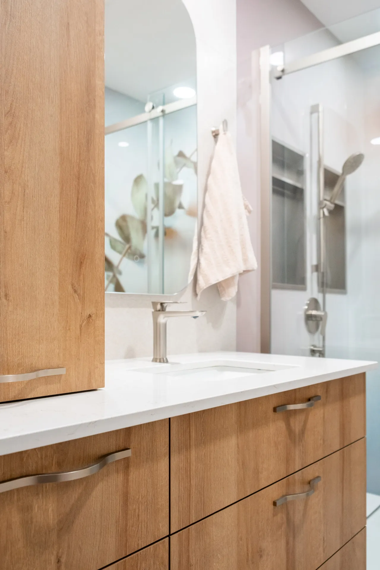 Salle de bain Forand: armoires en bois clair, comptoir blanc, miroir encadré, luminaires chrome, dosseret rose pâle