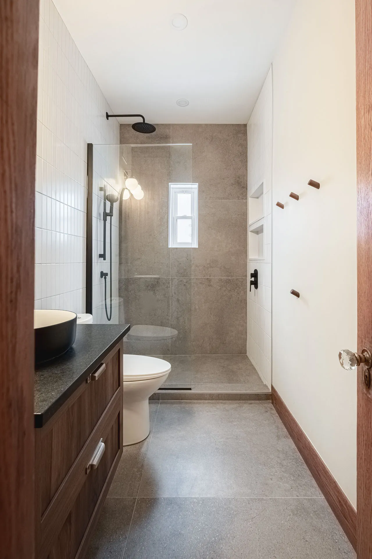 Modern bathroom with dark wood cabinetry, charcoal grey countertop, glass shower enclosure and beige tile