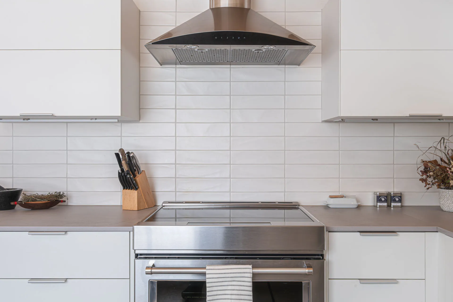 Modern Valière kitchen with white cabinets, grey countertop, white subway tile backsplash, central island and stainless hood