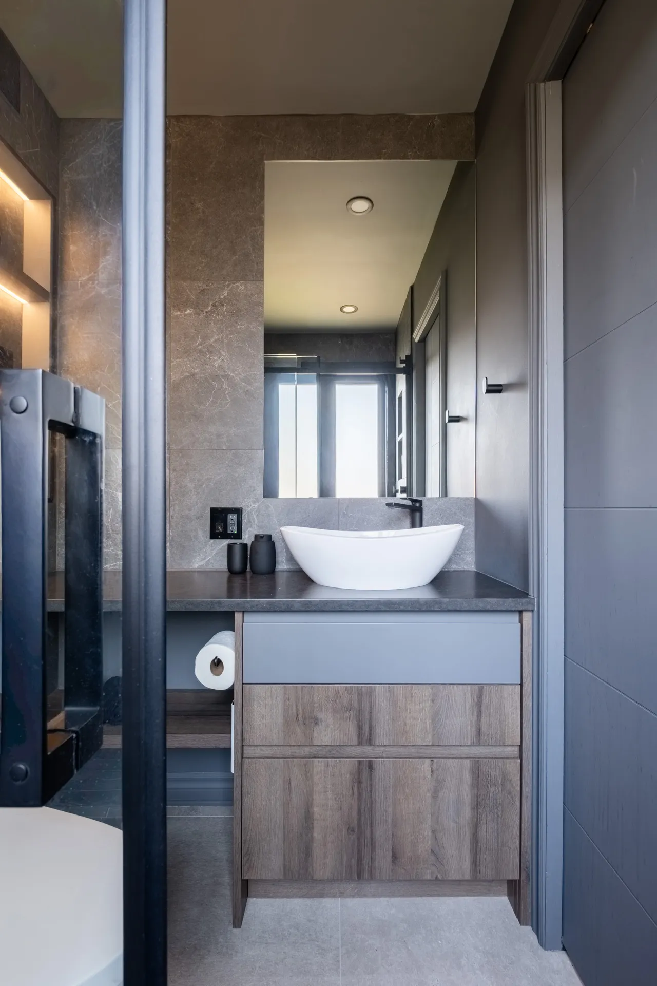 Salle de bain moderne avec vanité bois gris, comptoir gris foncé, lavabo blanc et miroir intégré